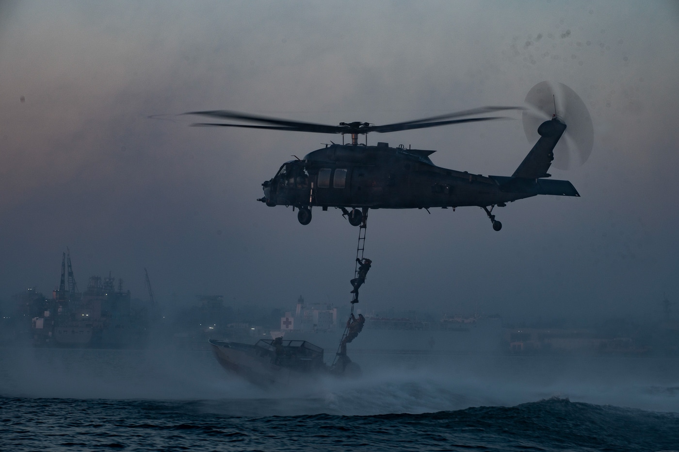 The image shows West Coast-based Naval Special Warfare operators climbing a caving ladder from a small combatant craft onto an MH-60M Black Hawk helicopter, which is assigned to the 160th Special Operations Aviation Regiment (Airborne). The operators, dressed in tactical gear and life vests, are ascending the ladder while the helicopter hovers just above the water’s surface. The maritime setting is clear, with waves and the boat in the background. This training evolution demonstrates the seamless integration between Navy special operations forces and the Night Stalkers. The photo emphasizes the coordination required for maritime insertion and extraction, a skill critical for special operations missions. Both the helicopter crew and the operators are focused on precision and safety. The scene illustrates the advanced training and joint capabilities of the 160th SOAR and Naval Special Warfare units.