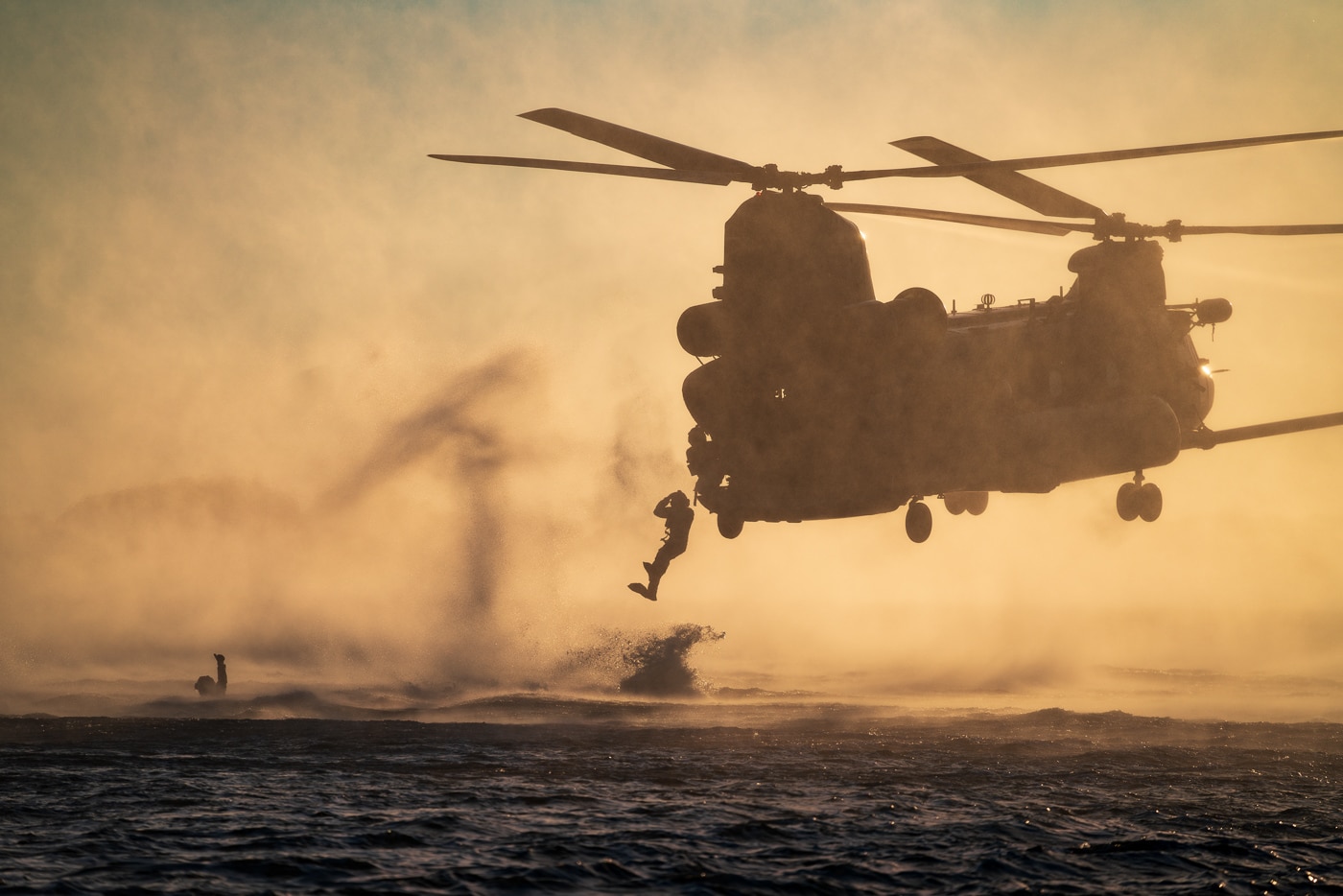 The image captures USAF Special Tactics Operators exiting an MH-60M Black Hawk helicopter in flight over water, a maneuver known as helocasting, with the helicopter operated by the 160th Special Operations Aviation Regiment (Airborne) out of Hurlburt Field, Florida. Operators, dressed in full tactical and flotation gear, are seen jumping or preparing to jump from the open doors or ramp of the hovering helicopter. The water below is calm or slightly rippled, and the horizon may include coastline or other elements indicating a training area. The MH-60M is stable and low to the surface, a hallmark of precision flying by the Night Stalkers. This joint training operation demonstrates the integration between Army aviation and Air Force special operations forces. Helocasting is used to insert personnel into maritime or riverine environments where traditional landing is impossible. The photo showcases both the teamwork and the technical expertise required for these complex missions.