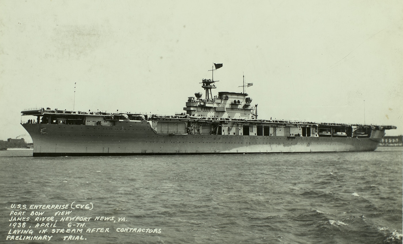 This photo shows USS Enterprise (CV-6) at sea during her initial trials, taken shortly after her completion and before entering active Navy service. The carrier displays her original paint scheme and uncluttered flight deck, with minimal equipment or aircraft visible. The ship’s island superstructure, flight deck markings, and hull number are prominent, illustrating her as-built condition. Calm waters and clear skies provide an unobstructed view of her full profile as she moves at moderate speed. The image highlights the sleek lines and balanced design of the Yorktown-class carriers before wartime modifications. These early sea trials were essential for testing propulsion, maneuverability, and all onboard systems prior to commissioning. This moment represents the very beginning of Enterprise’s long and decorated operational history.