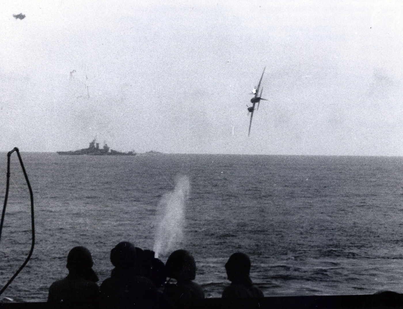 A wartime photo showing a Japanese Yokosuka P1Y “Frances” twin-engine bomber in a steep dive toward a U.S. Navy ship during a kamikaze mission in 1945. The aircraft’s wings are level, its nose angled downward, and faint smoke trails can be seen behind one engine. Anti-aircraft bursts dot the sky around the descending plane, and flashes of gunfire are visible from the ship below. The photo captures the tension and speed of a kamikaze attack in the Pacific theater. This image illustrates the use of heavy twin-engine aircraft for suicide strikes as Japan’s resources dwindled late in the war. The P1Y’s sleek design contrasts sharply with the destruction it carried into its final mission.