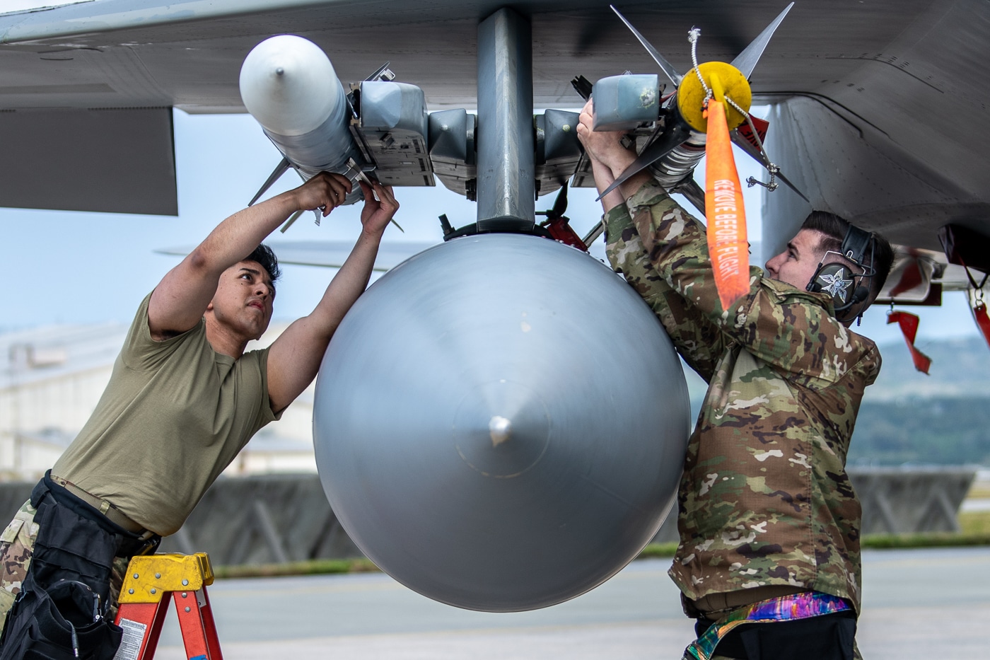 Senior Airman Kevin Arredondo and Staff Sgt. Bryor Moritz of the 44th Aircraft Maintenance Unit are shown loading ordnance onto an F-15C Eagle assigned to the 44th Fighter Squadron during the Shogun Showdown competition at Kadena Air Base, Japan, on February 3, 2023. Both Airmen wear standard maintenance uniforms, protective gloves, and communication headsets as they work beneath the fighter’s wing. The event tests the speed, accuracy, and teamwork of weapons load crews under simulated operational pressure. The F-15C, with its gray fuselage and twin tails, serves as the centerpiece for the competition. Kadena Air Base, located on Okinawa, is a key site for U.S. air operations in the Indo-Pacific. The image captures the attention to detail and technical expertise required to maintain combat readiness. It reflects the professionalism and precision of Air Force maintenance teams.