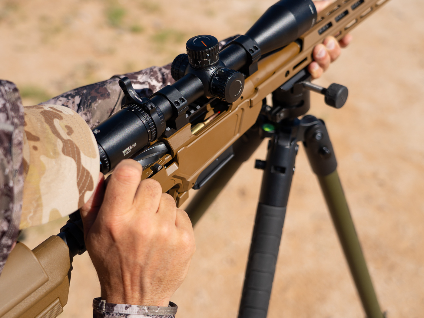 Shooter operating bolt action of Springfield Model 2020 Heatseeker precision rifle during range session demonstrating cycling process between shots. The spiral fluted bolt with dual lugs visible as shooter pulls rearward to extract fired cartridge case from chamber. EDM wire cut raceways in action provide smooth bolt travel with minimal friction during operation. Shooter maintains shooting position behind rifle while working bolt to chamber next round from AICS magazine. Carbon fiber barrel with mounted suppressor extends forward while Vortex scope remains at eye level. Bolt features 4140 steel construction with nitride finish for durability and corrosion resistance. The action lockup feels tight and precise contributing to rifle's exceptional accuracy performance. Shooter experienced smooth bolt manipulation throughout testing session producing sub-MOA groups with factory ammunition. Coyote Brown Cerakote chassis visible with M-Lok rail system and adjustable B5 precision stock.