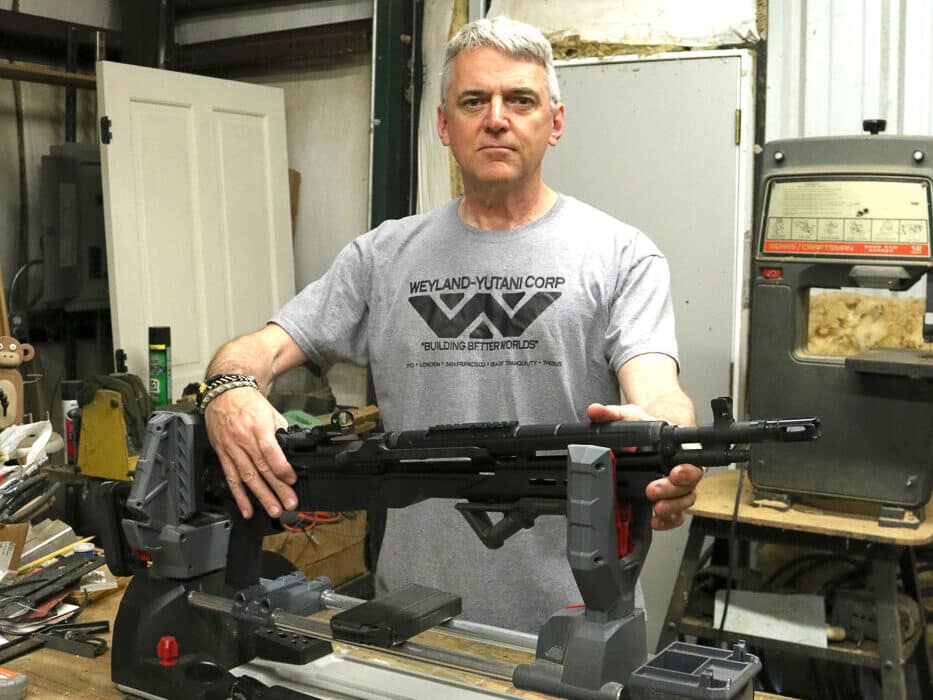 Author working with Springfield Armory M1A SOCOM rifle equipped with Delta 14 Chassis Gen 2 in workshop environment demonstrating the user-friendly installation process. The drop-in chassis system requires no permanent modifications to the firearm and can be installed by anyone capable of field stripping their rifle. Visible are the glass-filled polymer construction, M-Lok accessory slots, and the flared magwell that characterizes the Gen 2 design. The Mossberg 500 pattern mount at the rear provides compatibility with numerous aftermarket buttstock options for customization. The lightweight 0.75-pound chassis dramatically reduces overall rifle weight compared to traditional wood furniture. Workshop setting illustrates the home-gunsmith accessibility of this upgrade path for M1A owners seeking improved portability and modern features.