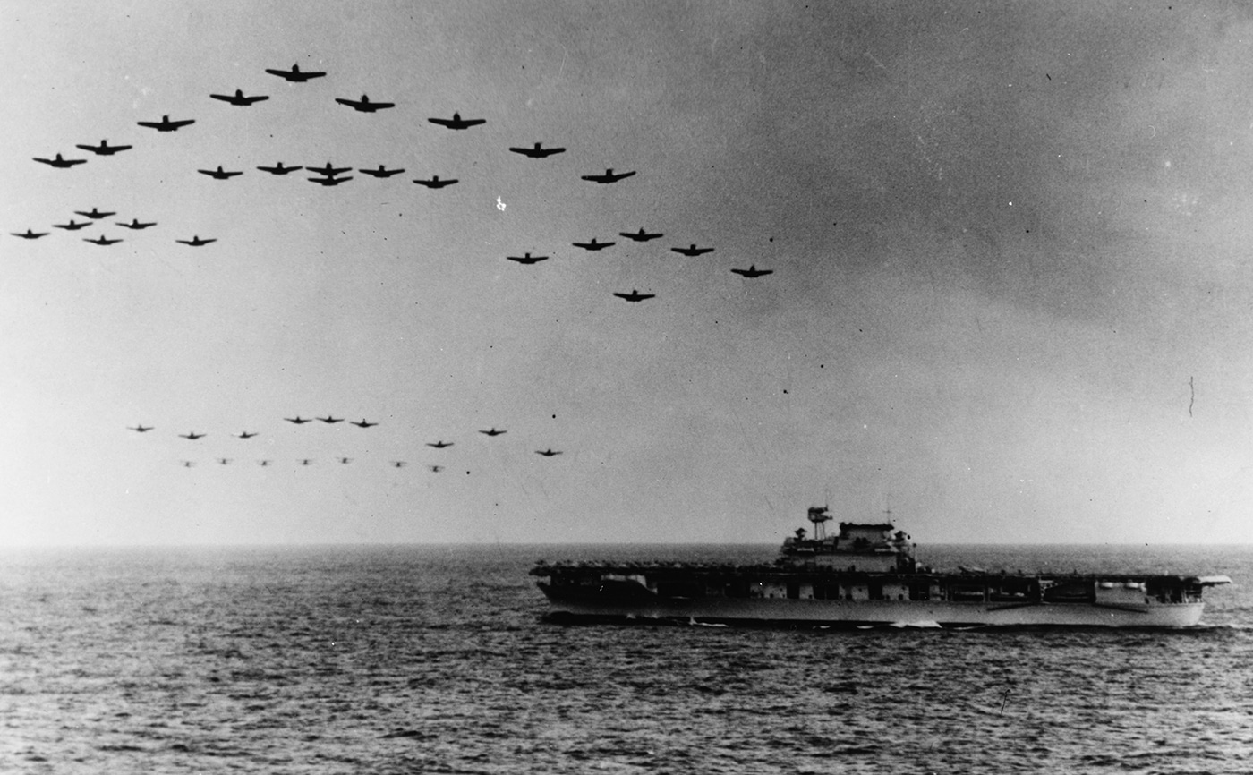 This photo shows a formation of carrier-based aircraft flying directly over USS Enterprise (CV-6), likely during a routine training exercise or operational display. The aircraft, including fighters and bombers, are arranged in tight formation above the ship’s flight deck. Below, the carrier is underway, with its flight deck mostly clear and crew members visible observing the spectacle. The image highlights the seamless coordination between the air wing and the ship’s crew, both essential for launching and recovering aircraft during combat missions. The shadow of the planes is visible on the deck, illustrating their proximity to the ship. This type of flyover was both a morale booster and a demonstration of the carrier’s offensive capabilities. The photo provides a vivid sense of the power and organization required for fleet carrier operations during World War II. USS Enterprise’s air group flew a range of missions, from air superiority to strike and reconnaissance, supporting every major campaign in the Pacific.