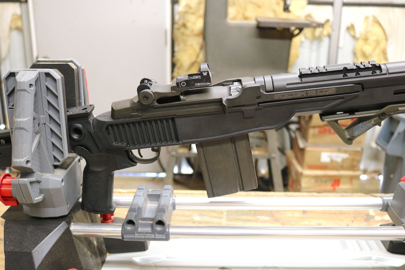 Close-up view of Delta 14 Chassis Gen 2 installation process showing M1A barreled action being seated into glass-filled nylon chassis during workshop assembly. The drop-in design requires trigger group removal from factory configuration followed by action placement into the new chassis system. Intentionally tight fit ensures rock-solid interface between rifle components and chassis maintaining accuracy and zero under recoil stress. Steel front ferrule visible in detail provides critical reinforcement where the barrel interfaces with the lightweight polymer construction. No permanent modifications to the M1A action are necessary and installation can be reversed to return rifle to original configuration. M-Lok slots along forend and flared magwell are visible showing the chassis features that enhance tactical functionality. The simple 5/16x18 fastener system at rear accepts Mossberg 500 pattern buttstock options. Installation requires only basic field stripping knowledge and common tools found in most gun owners' workshops.