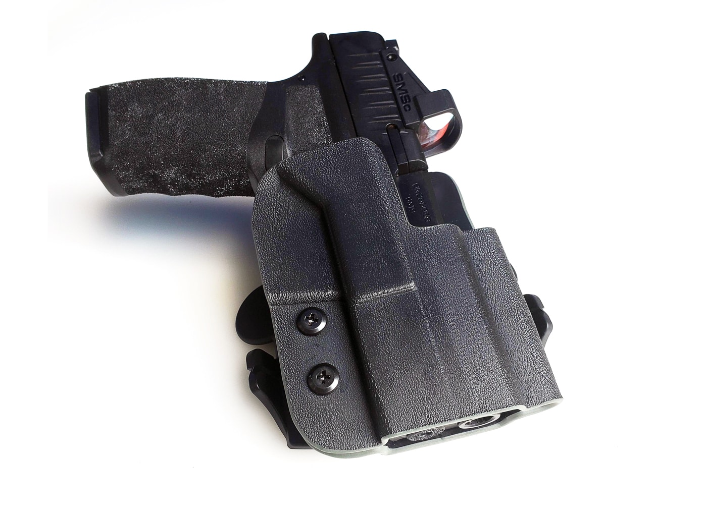 A Springfield Hellcat compact pistol seated in an outside-the-waistband paddle holster, photographed from a three-quarter angle. The molded holster body fully covers the slide and trigger guard while the wide polymer paddle fits inside the waistband and presses against the hip. This paddle holster provides passive retention with adjustable screws to fine-tune how tightly the Hellcat is held. The image highlights the paddle’s curved shape that distributes weight and keeps the holster stable during movement. This setup is commonly used for concealed carry under a jacket and for quick on/off range trips. Keywords: Springfield Hellcat, paddle holster, OWB holster, compact pistol, retention, concealed carry. The clear view of the draw path shows how the pistol will be accessed in a practical carry position.