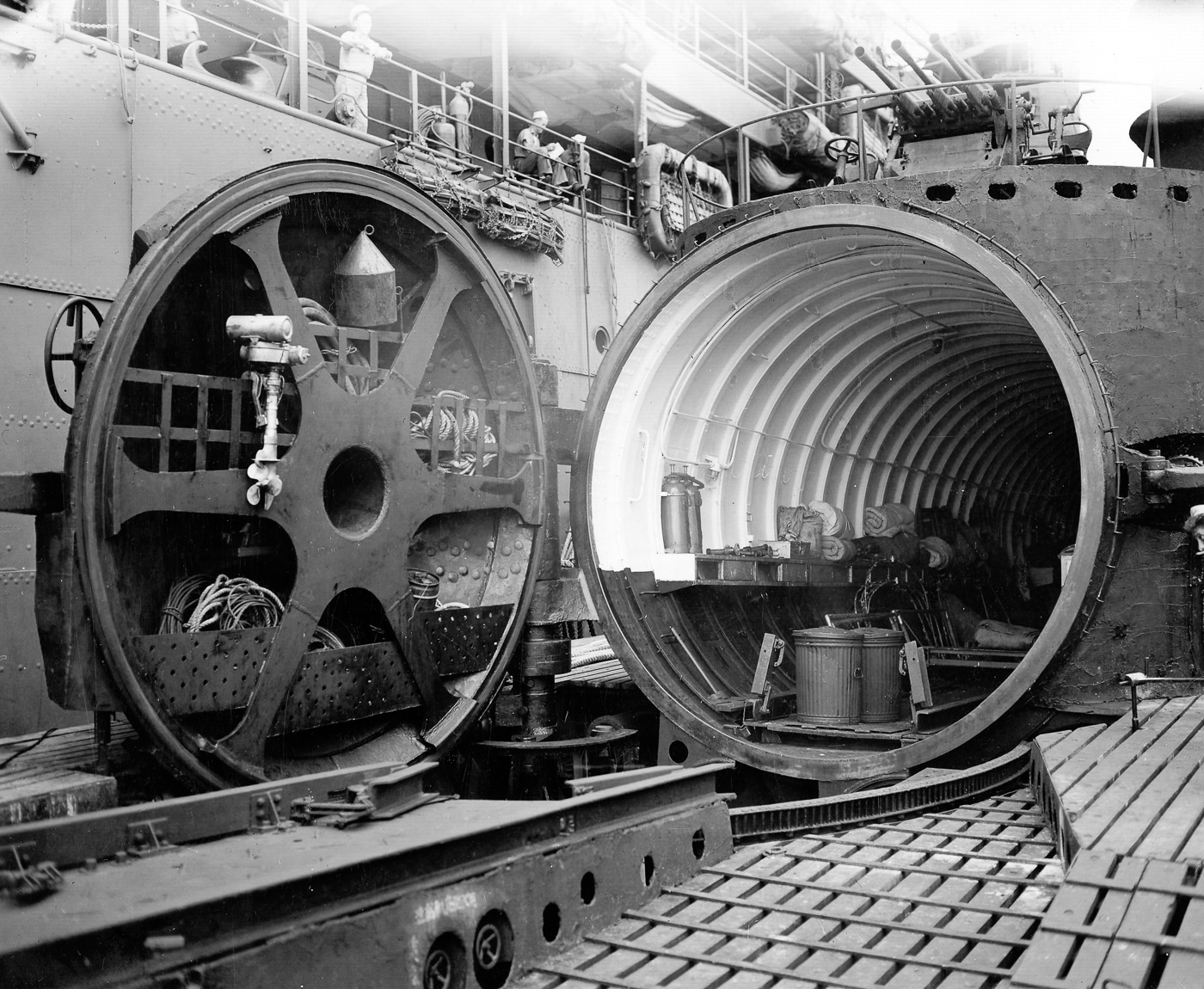 A black-and-white photo showing the forward section of the Imperial Japanese Navy submarine I-14, featuring a full view of the massive watertight hangar door. The door is sealed with a 2-inch-thick rubber gasket designed to protect the aircraft stored inside from seawater and pressure. Mounted on the conning tower deck above the hangar are triple 25mm Type 96 anti-aircraft autocannons, positioned to defend the submarine during surfacing and aircraft launch operations. The image illustrates the complexity of Japan’s I-class submarines, which combined aviation storage, catapult systems, and heavy defensive armament in a single vessel.
