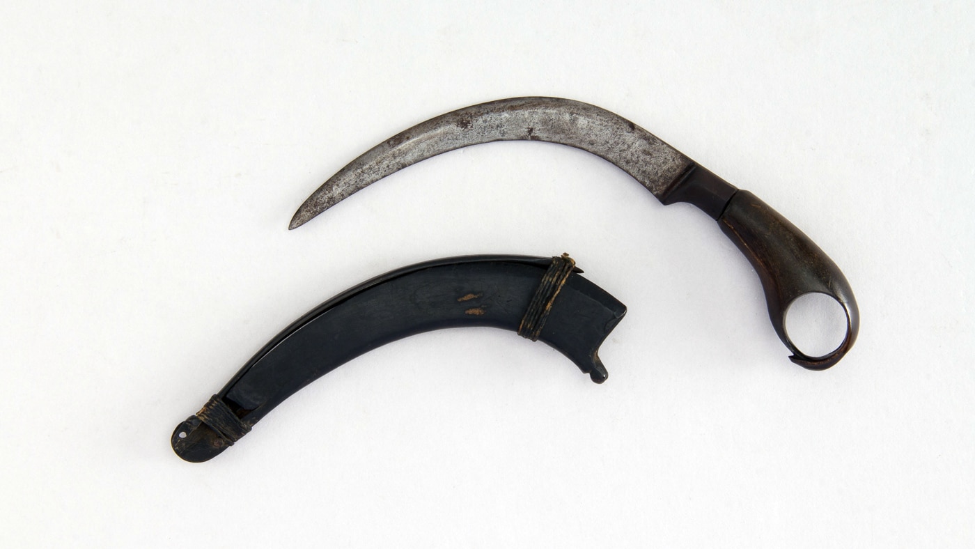 Photo of a 19th-century Malayan or Sulawesi kerambit with its original sheath. The curved, claw-like blade and ringed handle show the traditional form that inspired modern designs such as the Toor Knives Karsumba R. The materials appear to be aged wood and metal, displaying craftsmanship typical of Southeast Asian blades from that era. This image ties into the article’s historical overview of the karambit’s evolution from an agricultural tool to a close-combat weapon. It visually bridges the past and present, showing where modern tactical knives draw their lineage.