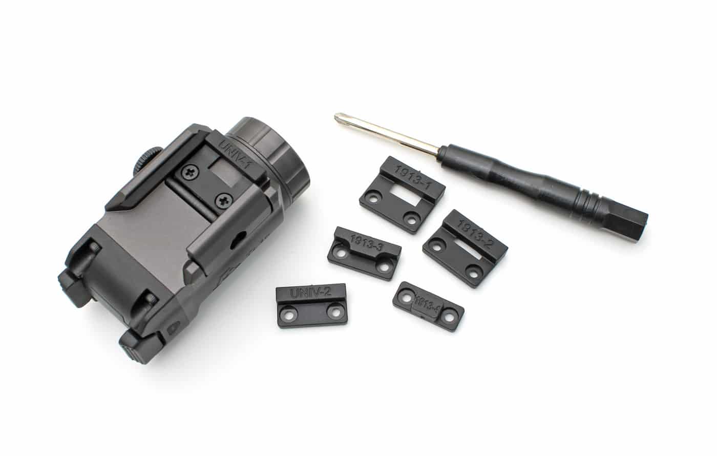 Photo of the GRITR TL1c Compact Weapon Light surrounded by an assortment of included rail spacers and adapters, laid out to show the options provided for fitting the light to different handgun rails. Each spacer is designed for specific brands or models, ensuring that users can achieve a secure and proper fit on a variety of pistols. This detail supports the article’s focus on the TL1c’s versatility and user-friendly setup, making it suitable for almost any defensive handgun. The light and spacers are arranged neatly, with some spacers labeled or differentiated by size and shape.