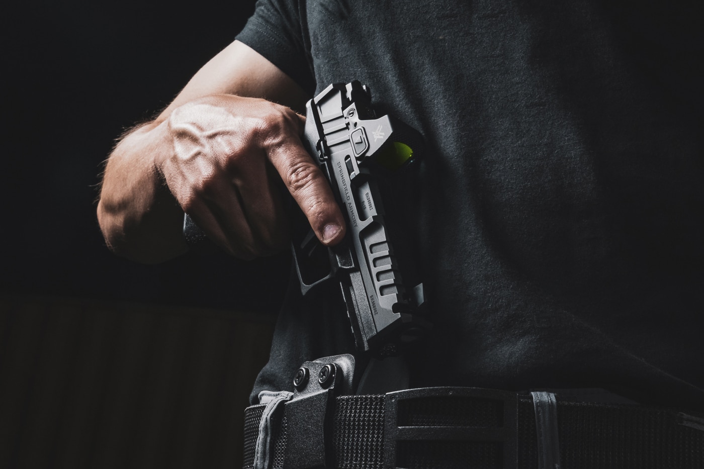 A man draws a 9mm pistol from an inside-the-waistband (IWB) holster, demonstrating a practical self-defense skill relevant to surviving a gunfight. The image highlights the importance of preparation, training, and composure in high-stress scenarios involving lethal threats. The photo is intended to illustrate fundamental skills recommended in discussions about gunfight survival, self-defense, and personal safety. The individual’s focused posture reflects the mental and physical readiness that is often emphasized in defensive training. The scene is neutral and avoids any sensationalism, making it suitable for educational content about self-defense principles. This type of image supports articles or resources on responsible firearm handling and effective response to imminent danger. Core topics include competency, consistency, and the ability to remain unflustered during emergencies.