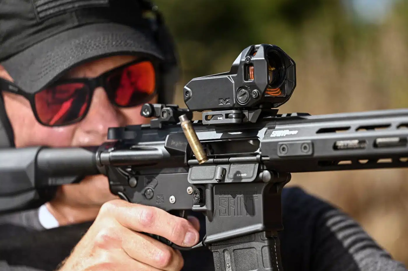 A uniformed officer is shown shooting a Springfield Armory SAINT AR-15 at an outdoor range, demonstrating a standard patrol rifle firing position. The shooter wears eye and ear protection and holds the rifle with a controlled, two-handed grip to manage recoil and maintain accuracy. The SAINT AR-15 is fitted with a red-dot optic, a weapon light, and a sling, illustrating a typical duty configuration available through Brownells’ law enforcement discount program. Nearby on the bench are spare magazines and a small tool kit, suggesting maintenance and readiness. The background shows the impact berm and lane markers common to police training ranges. This image conveys practical training, duty preparedness, and the types of accessories officers can purchase with verified LE pricing. The scene emphasizes safe firearm handling, professional gear choices, and the patrol-rifle role in modern policing. Brownells first responder discount is available to verified law enforcement officers and mirrors the Brownells military discount.