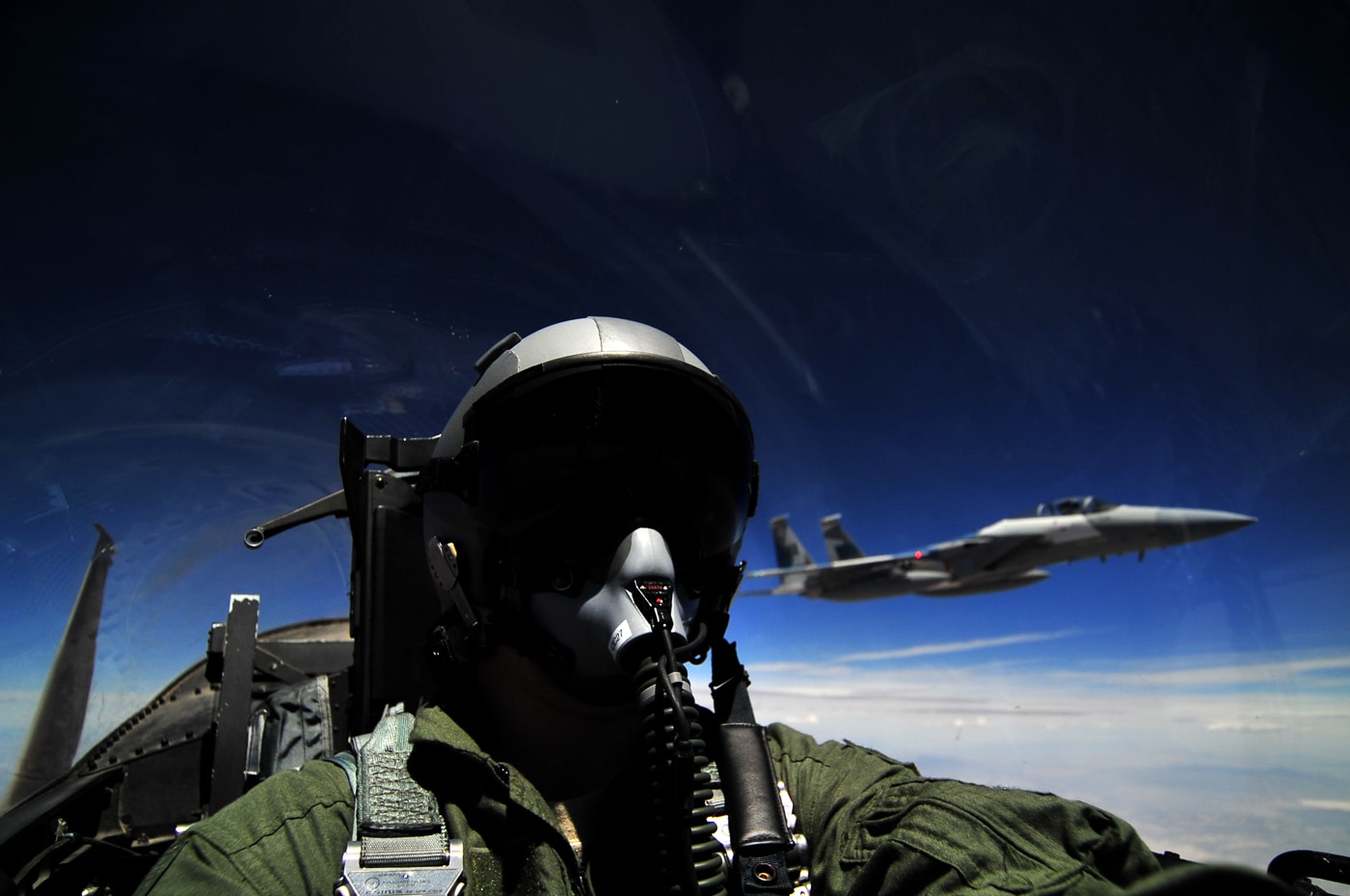 A U.S. Air Force pilot takes a self-portrait while flying an F-15D Eagle during a training mission. The pilot wears a flight helmet, oxygen mask, and visor, with cockpit instruments and the canopy clearly visible. Sunlight reflects across the glass, revealing a high-altitude view of the sky and terrain below. The F-15D is the two-seat training version of the McDonnell Douglas F-15 Eagle, used for both instruction and combat readiness exercises. This photo captures the intensity and focus required to operate one of the world’s most advanced fighter jets. The image emphasizes the precision of modern aircrew training and the human experience behind advanced military aviation.