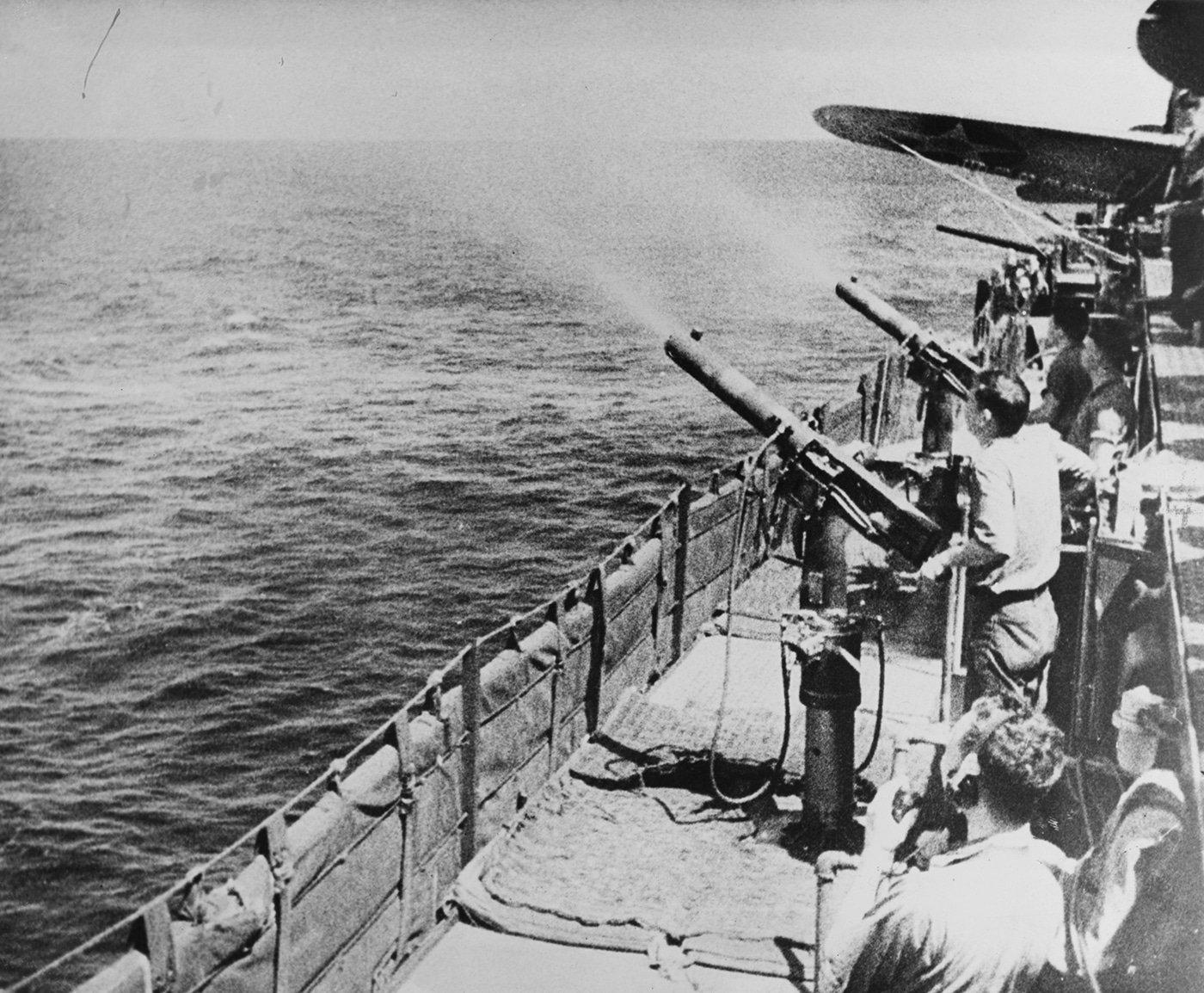 This photo shows several sailors manning .50-caliber machine guns on the deck of USS Enterprise (CV-6) as the carrier participates in a raid on the Marshall Islands in February 1942. The gun crews are positioned behind their weapons, scanning the skies and horizon for enemy aircraft. The scene is tense, with gunners wearing helmets and life vests as they prepare to engage potential threats. The ocean is visible in the background, with the ship underway and ready for action. The machine guns are mounted along the edge of the flight deck, with ammunition belts loaded and ready. This was one of the first major U.S. carrier strikes in the Pacific, marking a shift to offensive operations against Japanese-held territory. The image highlights the crucial role of anti-aircraft defense and the constant readiness required from every crew member. It provides a close-up look at the early-war defensive measures aboard USS Enterprise.