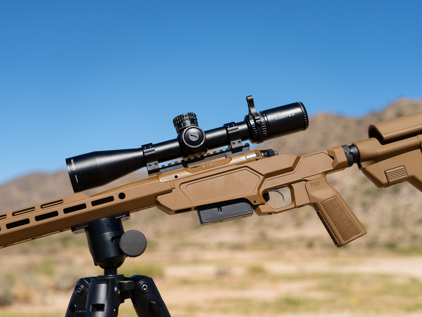 Vortex Viper PST 3-15x44 riflescope mounted on Springfield Model 2020 Heatseeker precision rifle showing magnification range suitable for shooting to 500 yards and beyond. The scope features first focal plane EBR-7C MRAD reticle allowing holdovers without dialing turrets for quick target engagement. Optic mounted in quality rings on Picatinny rail with dual recoil pins ensuring zero retention. The 44mm objective lens provides sufficient light gathering while keeping overall scope weight reasonable. Magnification range of 3-15 power covers close range work through extended distance precision shooting. Vortex Viper PST known for excellent clarity and consistency at its price point making it popular choice for precision rifles. Reticle design with hash marks and wind holds simplifies ranging and compensation at distance. This scope contributed to first-round hits on steel plates extending to 500 yards during testing. Coyote Brown chassis visible below optic with carbon fiber barrel extending forward.