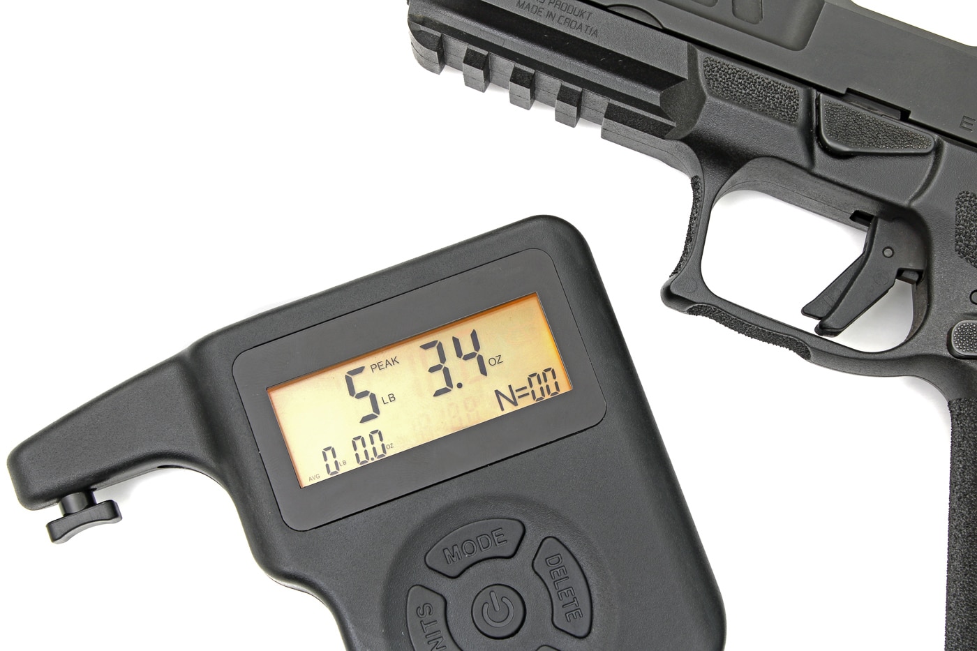 The photograph shows a close-up of the trigger area of a Springfield Armory Echelon pistol with a digital trigger gauge hooked to the trigger face, the readout displaying approximately 5 lb 3 oz. This image documents the measured trigger pull weight for California-compliant Echelon pistols and is intended to clarify the actual force required to fire the striker-fired platform. The trigger face, trigger guard, and part of the textured grip are visible, giving context for finger placement and reach. The captioned reading supports editorial text describing a crisp, duty-grade trigger with a short, tactile reset. Mention of a magazine disconnect safety and loaded chamber indicator appears in the article, but the photo focuses solely on the external trigger measurement.