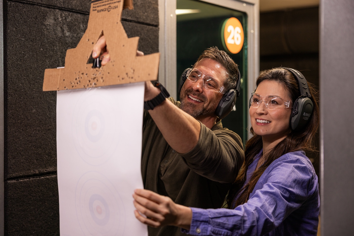 Photo of two Range USA customers preparing for an afternoon of shooting inside a modern indoor range. Both individuals are wearing hearing and eye protection while setting up paper targets at the far end of their lanes. The facility features clean, well-lit shooting booths separated by safety barriers, with visible range equipment and signage. The shooters appear focused but relaxed, taking time to ensure their targets and firearms are properly arranged. The environment shows Range USA’s emphasis on safety, order, and comfort for all experience levels. The image reflects how each facility provides a reliable and consistent shooting experience nationwide.