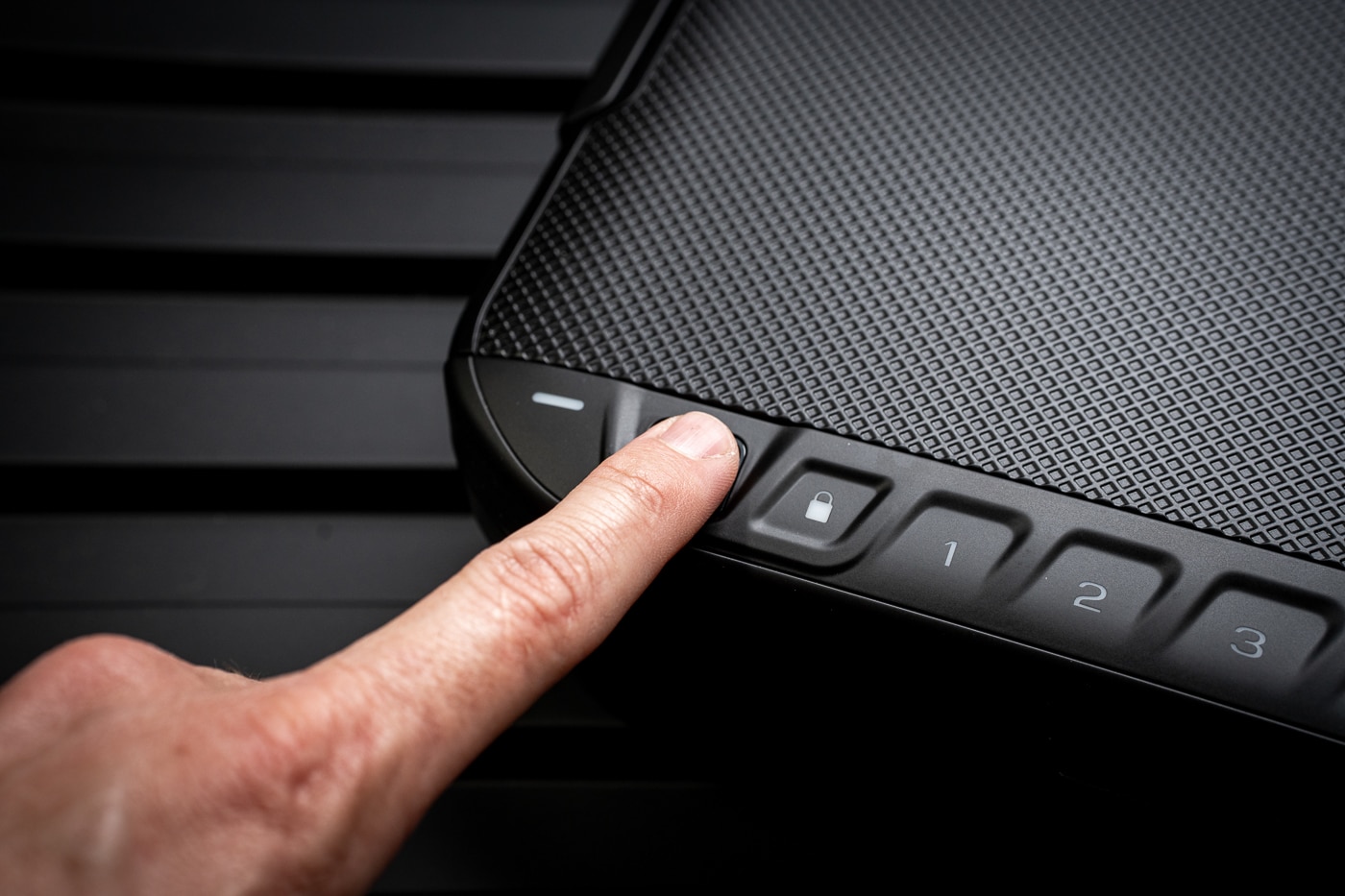Image showing a close-up of a pointer finger engaging the fingerprint reader on the LifePod 20, used as a demonstration in a Vaultek Lifepod 20 Biometric review. The fingerprint pad is on the case lid next to the keypad, and the LED ring around the scanner is faintly lit, suggesting an active read. The focus is tight on the finger and scanner to illustrate how the biometric system recognizes stored prints for quick opening. Background elements like the latch and case edge are visible enough to show the unit’s compact size and travel-ready design. This ALT text helps screen-reader users understand that the photo demonstrates biometric unlocking, fingerprint access, and the user-friendly interface of the portable safe. It also uses related keywords  —  biometric scanner, fingerprint unlock, travel safe  —  to aid SEO.
