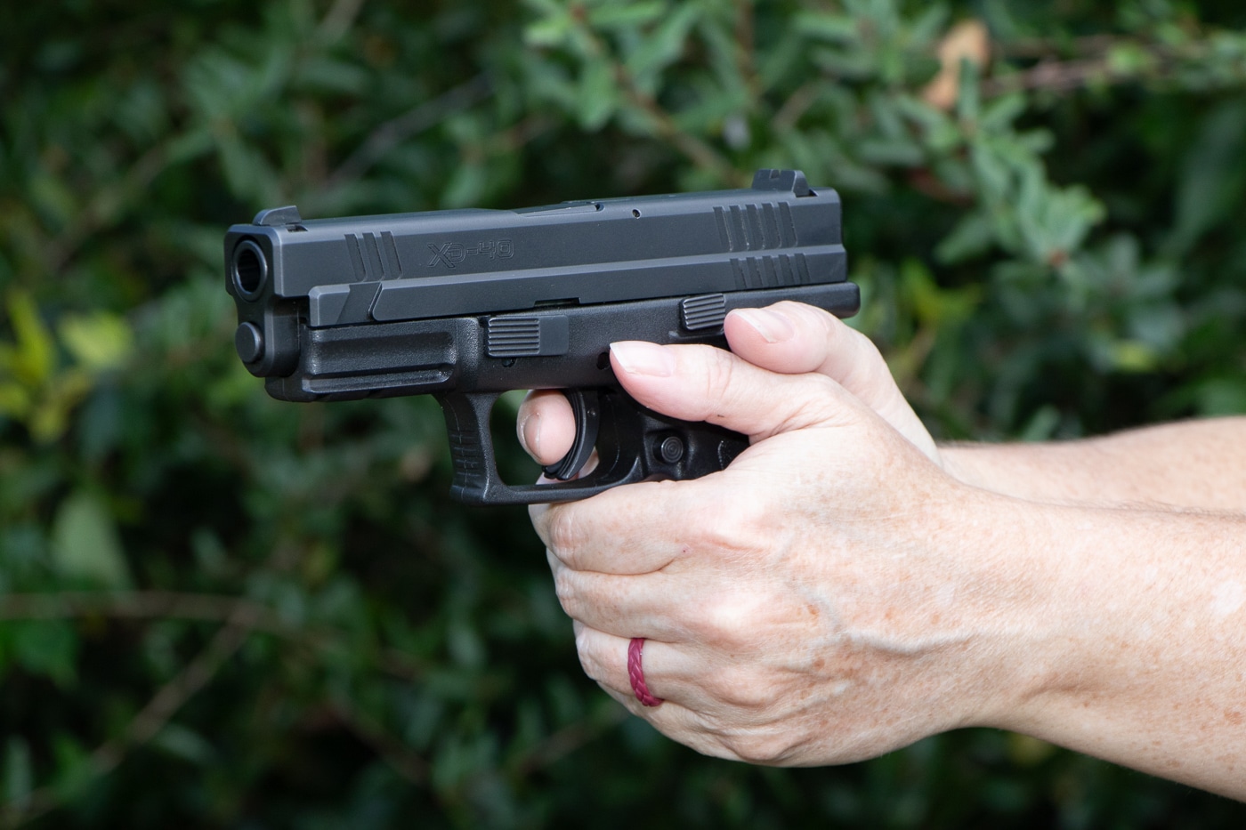 Female shooter pressing trigger on Springfield XD striker-fired pistol after feeling trigger reset click demonstrating proper finger position at reset threshold. Understanding how trigger reset works mechanically in striker-fired handguns where disconnector releases sear to allow re-engagement after firing shot. Shooter maintains trigger contact at reset point rather than full forward travel to minimize finger movement between rapid fire shots. Springfield XD reset distance allows faster follow-up shots by keeping trigger finger positioned where mechanical components have re-engaged and firearm is ready to fire again. Proper trigger control technique at reset reduces disruption to sight alignment and grip stability.