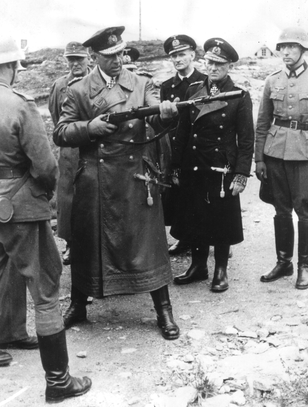 German Admiral Otto Ciliax test fires a Mauser Karabiner 98k rifle fitted with the Schiessbecher rifle grenade launcher during a coastal inspection of Wehrmacht defensive positions in occupied Norway during World War 2. The senior Kriegsmarine officer handles the Kar98k bolt-action rifle equipped with the cup-style Gewehrgranatengerät launcher that allowed German infantry to fire anti-tank Panzergranate and fragmentation grenades from their standard 7.92x57mm service rifles. Norwegian coastal defenses manned by Wehrmacht troops received regular inspections from German military leadership throughout the occupation from 1940 to 1945, with officers evaluating weapons, fortifications, and troop readiness against potential Allied amphibious assault. The Schiessbecher launcher mounted on the Karabiner 98 kurz muzzle gave German soldiers defending Norway's extensive coastline the ability to engage landing craft and armored vehicles with rifle-launched explosive projectiles. Admiral Ciliax served in prominent Kriegsmarine roles including command of capital ships during the famous Channel Dash operation in February 1942 when Scharnhorst, Gneisenau, and Prinz Eugen escaped from Brest through the English Channel. German cross-service cooperation meant naval officers frequently inspected and coordinated with Wehrmacht ground forces, particularly in coastal defense sectors where Kriegsmarine and army units worked together defending occupied territories. The rifle grenade system on the Mauser 98k provided squad-level indirect fire capability without requiring dedicated mortar teams or heavy weapons, making it valuable for dispersed defensive positions along Norway's rugged terrain. Wehrmacht soldiers stationed in Norway used the Karabiner 98k as their primary infantry weapon throughout the occupation, with the Schiessbecher launcher attachment enhancing their ability to defend beaches, fjords, and coastal installations against Allied commando raids and potential invasion forces.