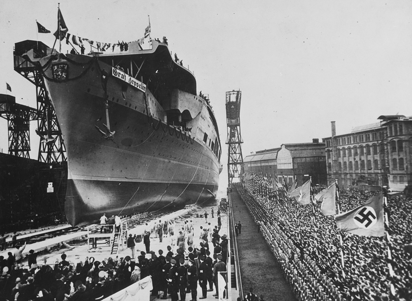 Launching ceremony German aircraft carrier Graf Zeppelin Kiel Germany 1938 Kriegsmarine flattop construction Nazi warship development Third Reich naval program. Hitler's carrier Graf Zeppelin-class vessel displacement 33550 tons length 262 meters beam 31 meters designed speed 35 knots. German carrier program Deutsche Werke shipyard slipway construction incomplete aircraft carrier never commissioned never operational. Kriegsmarine naval aviation ambitions flattop warship Graf Zeppelin named Count Ferdinand von Zeppelin rigid airship inventor. Nazi Germany carrier construction World War II German naval forces Atlantic theater operations surface raiding fleet expansion plans.