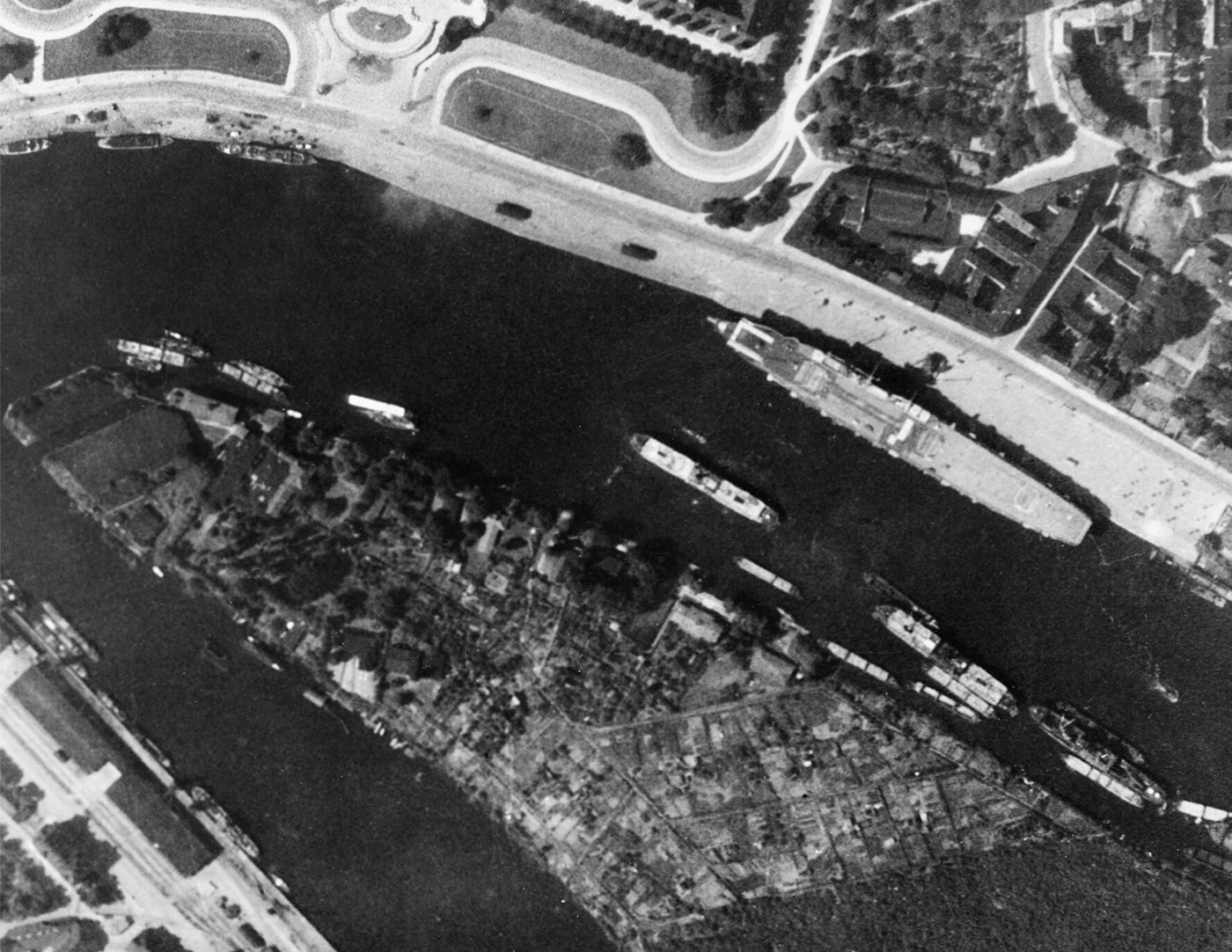 German aircraft carrier Graf Zeppelin moored Oder River Stettin Germany World War II showing incomplete Kriegsmarine flattop alongside West bank near Nusche shipbuilding works. Hitler's carrier Graf Zeppelin relocated multiple times avoid British Royal Air Force bombing raids Soviet air attacks. Nazi warship construction halted 1943 incomplete aircraft carrier used storage depot. Kriegsmarine flattop Graf Zeppelin displacement 33550 tons never completed never operational Third Reich naval program. German carrier Stettin port East Prussia wartime relocation strategy protect unfinished warship enemy air raids Atlantic theater World War II.