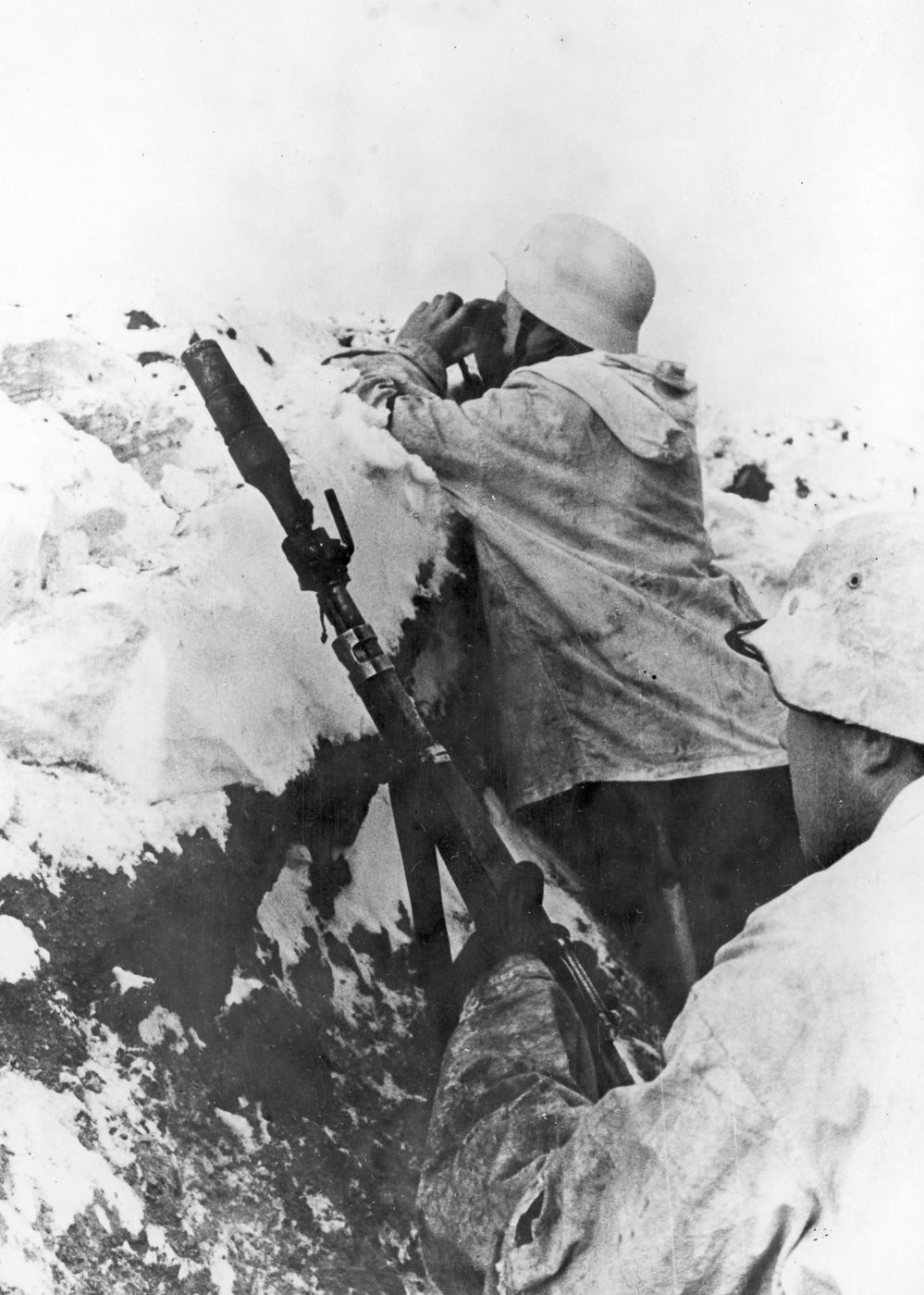Eastern Front combat scene showing a German rifle grenade team in a defensive trench with one Wehrmacht soldier aiming a Karabiner 98k fitted with a Schiessbecher launcher while his comrade uses binoculars to spot targets and adjust fire during operations against Soviet forces in World War 2. The grenadier holds the Kar98k bolt-action rifle at an elevated angle necessary for launching rifle grenades in high arcs toward enemy positions, using the Gewehrgranatengerät cup launcher mounted on the 7.92x57mm Mauser's muzzle. German infantry tactics emphasized coordinated fire team operations where spotters with optical equipment directed rifle grenade fire, providing range estimates and observing impact points to help gunners adjust subsequent shots onto Soviet troop concentrations or fortified positions. Trench warfare conditions on the Eastern Front from Operation Barbarossa in 1941 through the final battles in 1945 required German soldiers to maximize firepower from limited positions, making rifle-launched grenades valuable for engaging targets beyond direct fire range. The Karabiner 98 kurz rifle grenade system gave Wehrmacht infantry squad-level indirect fire capability without the weight and complexity of mortars, allowing individual two-man teams to provide supporting fire during defensive operations and assaults. Special grenade launching cartridges with wooden bullets propelled various projectile types from the Mauser 98k including high-explosive fragmentation rounds against Soviet infantry, Gewehr-Panzergranate shaped charges against T-34 tanks and armored vehicles, and smoke grenades for screening maneuvers. The spotter's binoculars allowed German soldiers to identify targets at extended ranges across the Eastern Front's vast open terrain, observing fall of shot and communicating corrections to the grenadier for improved accuracy on subsequent rounds. Wehrmacht rifle grenade doctrine trained soldiers to work as integrated teams where observation and fire adjustment were as important as the actual launching, reflecting German emphasis on combined arms tactics even at the smallest unit levels.