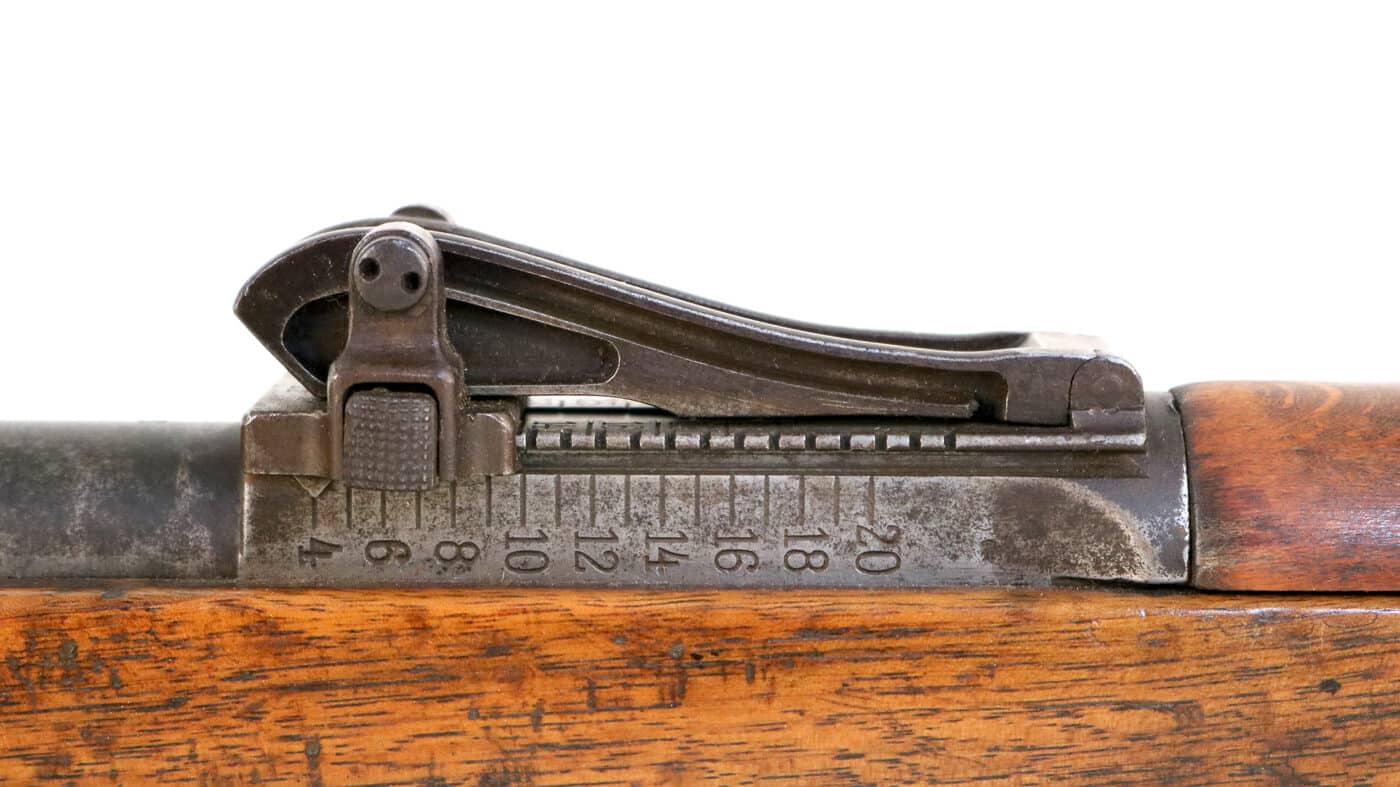 Close-up photograph of Lange Visier rear sight system on German Gewehr 98 bolt-action rifle showing complex tangent-style sighting device graduated from 200 meters to 2000 meters in 100-meter increments used by Imperial German infantry during World War I. The elaborate curved rear sight on Gew 98 rifle represents sophisticated German military engineering with adjustable elevation settings allowing soldiers to theoretically engage targets at extreme distances using 7.92x57mm Mauser S Patrone ammunition firing 154-grain Spitzer bullets. This complex Lange Visier sight mechanism on Gewehr 98 featured movable aperture and tangent graduations that German soldiers including Adolf Hitler and millions of infantrymen used from 1914-1918 though practical effective range with iron sights under combat conditions proved much shorter than theoretical 2000-meter maximum. The intricate rear sight design on G98 bolt-action rifle demonstrates German attention to precision engineering even if extreme range capability rarely proved useful during typical trench warfare engagements on Western Front and Eastern Front battlefields.