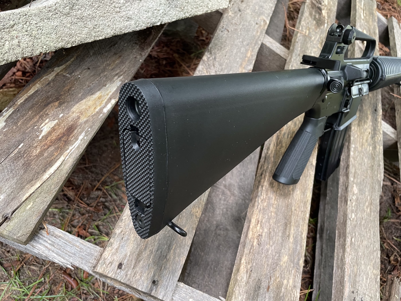 M16A2 rifle buttstock showing extended length of pull and textured buttplate improvements over shorter M16A1 stock design. A2 stock features toothy textured surface that prevents slippage from shoulder pocket unlike smooth buttplate on M16A1. Extended length of pull on M16A2 increased by 0.62 inches compared to frankly too short M16A1 stock for better shooting ergonomics. Stronger Zytel-type glass-filled thermoset polymer construction on A2 stock addresses durability concerns from weaker M16A1 material. Hinged trap door for cleaning rod storage retained from M16A1 design visible on M16A2 buttstock. Textured buttplate surface on A2 provides secure shoulder retention during recoil compared to slippery smooth plate on A1 variant. Stock modifications from M16A1 to M16A2 requested by Marine Corps after Vietnam War field experience identified need for better durability and fit. Component detail illustrates M16A2 improvements over M16A1 including longer stock, textured surface, and reinforced polymer material for enhanced reliability at 300 to 400 meter engagement distances.