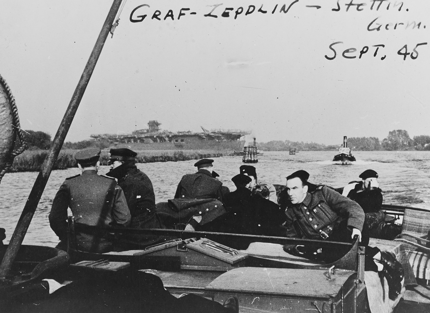 Soviet soldiers on a boat on River Oder in Szczecin with Graf Zeppelin aircraft carrier in background