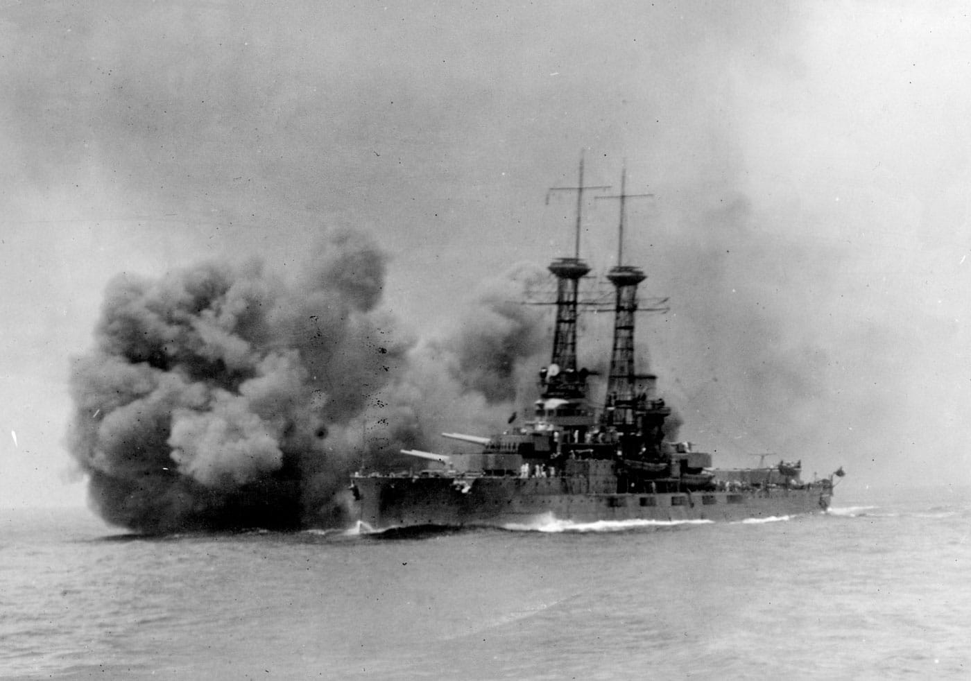 USS Delaware American dreadnought battleship firing her main guns during training exercise, representing one of two Delaware-class vessels that were the next generation of United States dreadnoughts with improved speed, size, and armament over the pioneering South Carolina-class battleships. The Delaware-class United States dreadnoughts consisted of USS Delaware BB-28 and USS North Dakota BB-29, both equipped with ten 12-inch guns providing increased firepower compared to the eight 12-inch guns on earlier American dreadnoughts. These second-generation American dreadnought battleships featured a maximum speed of 21 knots, addressing the speed limitations of the South Carolina-class vessels that could barely reach 19 knots, though they remained slower than many foreign battleships. The dramatic photograph captures USS Delaware firing her main battery during training operations, showing the immense firepower and combat capabilities of early 20th century United States Navy dreadnought battleships. The Delaware-class vessels were bigger in displacement and dimensions than the South Carolina-class, representing the continuing evolution of American dreadnought design as the U.S. Navy refined battleship construction techniques and incorporated lessons from earlier vessels. Both Delaware-class dreadnought battleships served during World War I, participating in naval operations and contributing to American sea power during the Great War alongside other United States battleships. The image shows the massive muzzle blast and smoke from USS Delaware's 12-inch guns, demonstrating why dreadnought battleships with their uniform all-big-gun batteries revolutionized naval warfare and made all pre-dreadnought mixed-caliber vessels obsolete. Both Delaware-class battleships were broken up during the Interwar period, victims of post-World War I budget constraints and eventually the Washington Naval Treaty that forced the United States Navy to reduce its battleship fleet by scrapping older capital ships.