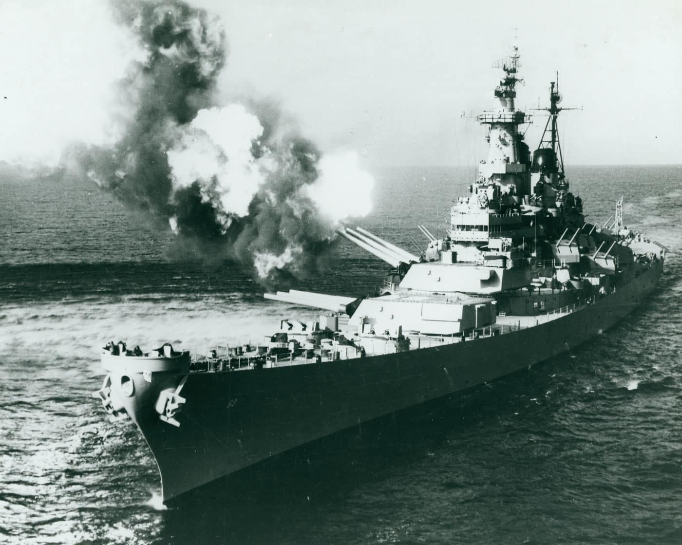 USS Missouri BB-63 American fast battleship fires a salvo of 16-inch shells from turret number 2 while bombarding Chongjin, North Korea in October 1950, demonstrating the devastating shore bombardment capability that kept Iowa-class battleships combat-relevant through multiple conflicts. USS Missouri BB-63 was one of four Iowa-class United States fast battleships including USS Iowa BB-61, USS New Jersey BB-62, and USS Wisconsin BB-64, all serving with distinction in World War II and continuing to prove their combat value during the Korean War. The dramatic photograph shows USS Missouri delivering accurate naval gunfire support against enemy communications targets in North Korea, illustrating why battleship shore bombardment remained critically important even as naval warfare increasingly emphasized aircraft carriers and submarines. USS Missouri BB-63 holds special historical significance as the site where Japan formally surrendered on September 2, 1945 in Tokyo Bay, ending World War II, making this battleship one of the most historically important vessels in United States Navy history. All four Iowa-class fast battleships served during the Korean War providing devastating shore bombardment, with their 16-inch guns capable of delivering accurate fire support from ranges exceeding 20 miles, supporting United Nations ground forces throughout the conflict. The Iowa-class battleships were fitted with nine 16-inch guns across three main turrets plus extensive secondary armament including 5-inch dual-purpose guns, demonstrating the concentrated firepower that made these fast battleships the most powerful capital ships ever built. USS New Jersey BB-62 would later serve during the Vietnam War, and in the 1980s all four Iowa-class fast battleships were modernized and returned to service with President Reagan adding Harpoon missiles, Tomahawk cruise missiles, and Phalanx systems alongside the refurbished 16-inch guns. These modernized Iowa-class battleships supported peacekeeping in Lebanon and provided shore bombardment during the Gulf War before final decommissioning in the 1990s, with USS Missouri now serving as a museum ship in Pearl Harbor alongside the USS Arizona memorial.