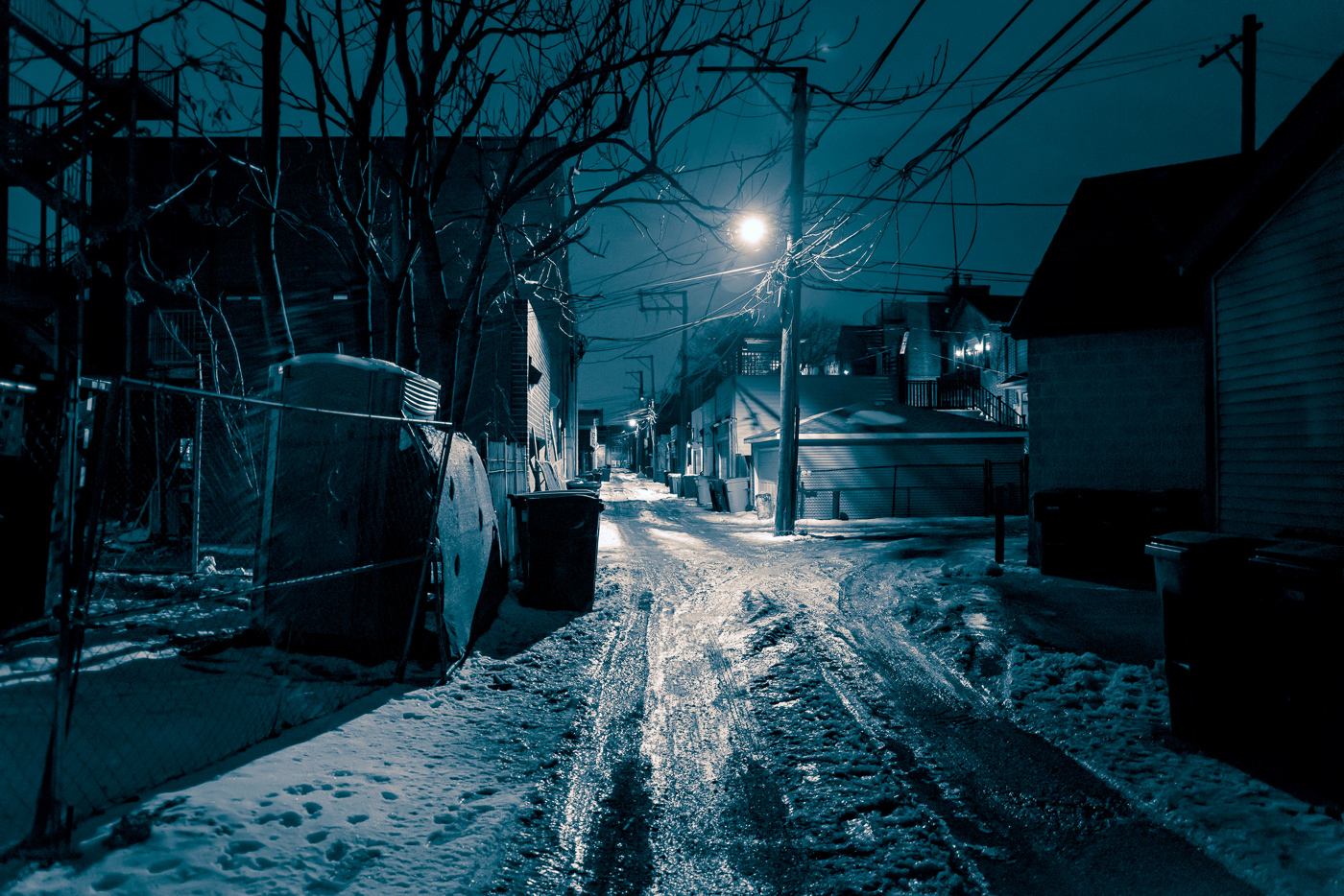 Abandoned residential street at night during winter showing icy road conditions and dark environment illustrating real-world cold weather concealed carry scenarios where reduced visibility and compromised footing affect defensive readiness and situational awareness. Photo depicts deserted urban winter street with ice coverage and sub-zero temperature conditions demonstrating environmental challenges that armed citizens face when carrying concealed firearms during northern states winter months or snow belt region cold snaps. Nighttime winter street scene showing slippery ice conditions that limit mobility and increase fall risk for concealed carriers wearing heavy winter coats and insulated clothing that already restrict range of motion and draw stroke capability. Image of dark residential area during freezing winter night illustrating threat assessment difficulties when visibility decreases and bulky winter layering systems slow reaction time for accessing holstered pistols in IWB or OWB carry positions. Cold weather urban environment at night showing icy streets where concealed carry permit holders must balance movement caution with maintaining hand positioning outside pockets for quick access to defensive firearms despite cold-induced discomfort. Winter night street photography depicting real conditions where CCW practitioners encounter combination of darkness, precipitation, ice hazards, and cold temperatures requiring tactical awareness of how heavy winter jackets, shooting gloves, and layered clothing affect presentation speed and combat grip establishment. Deserted nighttime winter street with ice and snow showing defensive scenario environment where concealed carriers must navigate slippery surfaces while maintaining situational awareness and accessibility to holstered Glock, Springfield, Sig Sauer, or Smith & Wesson pistols beneath multiple fabric layers and insulated cover garments from brands like Carhartt, 5.11 Tactical, or Vertx that provide concealment but introduce draw time complications.