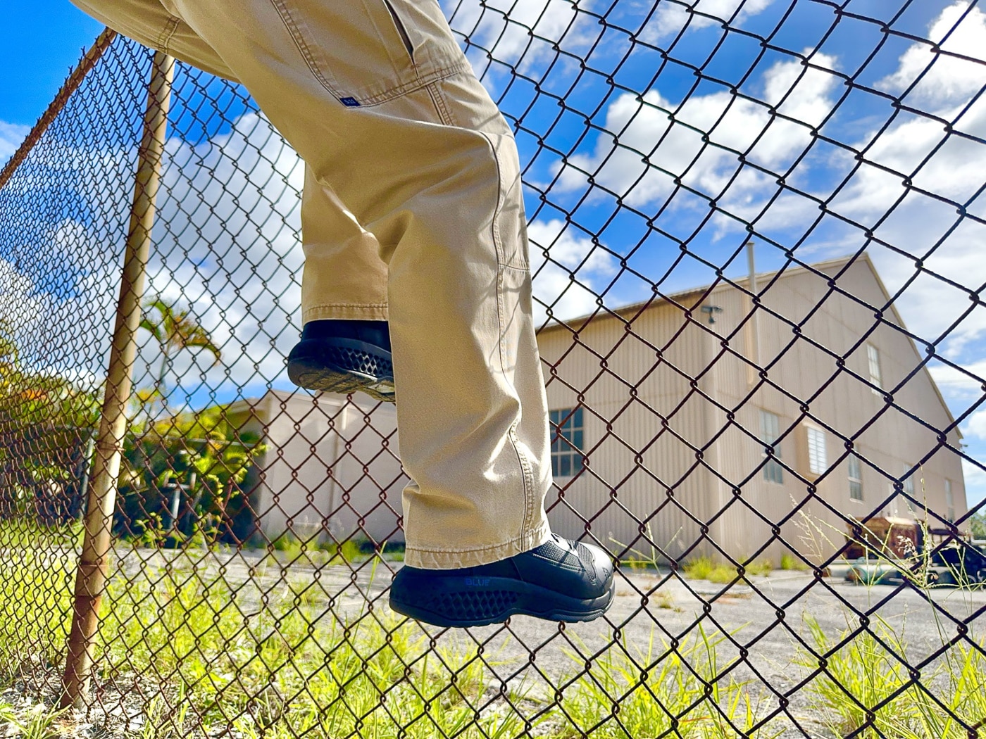 Police officer wearing Rocky Code Blue tactical duty boots outdoors showing six-inch height patrol boot performance during field evaluation by experienced law enforcement professional. Black tactical boots with breathable mesh upper and thermoplastic polyurethane TPU overlays worn during rigorous testing including circuit training and outdoor terrain navigation. Law enforcement footwear demonstrated on officer showing proper fit in normal shoe size with oval laces and padded collar providing secure comfortable wear for extended patrol shifts. Rocky Boots Code Blue public service footwear worn by K9 officer with extensive patrol experience evaluating budget-friendly tactical boot durability and functionality. Non-waterproof patrol boots shown in practical use avoiding swampy micro-environments common with waterproof boot designs that trap heat and moisture in warm climates. Six-inch tactical boots worn during high-stress activities including side-straddle hops calf raises push-ups and pull-ups testing boot construction and sole attachment integrity. Rocky public safety boots demonstrated by police professional showing oil and slip-resistant rubber outsole tread performance on varied surfaces from pavement to overgrown areas. Affordable law enforcement duty boots under $100 worn during real-world testing scenarios including fence climbing field searches and circuit training workouts simulating active patrol conditions.