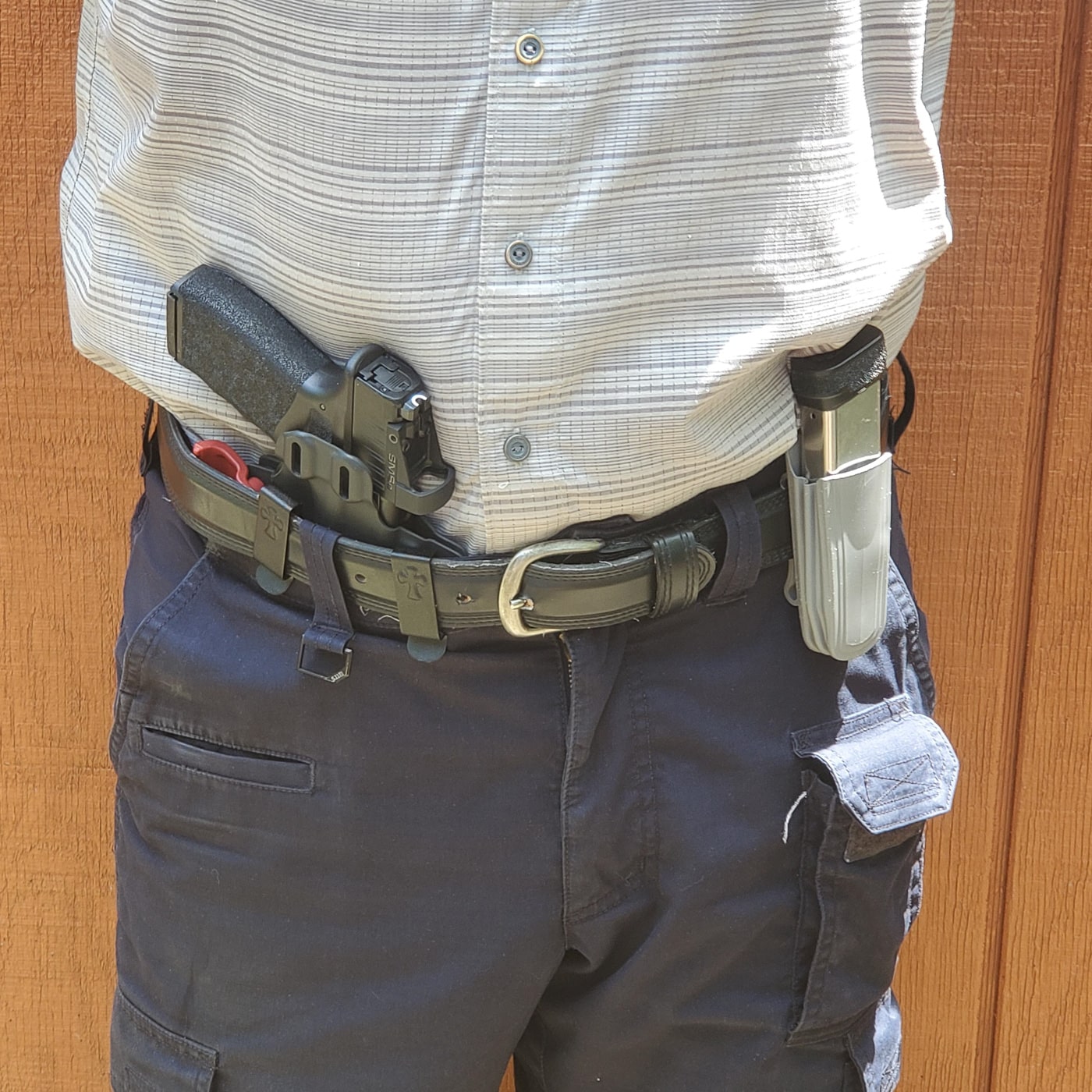 Author demonstrating concealed carry technique with a Springfield Hellcat pistol and spare magazine as part of his everyday carry self-protection setup. The compact defensive handgun sits in a quality holster positioned for effective draw stroke and threat response during emergency situations. The extra magazine carrier provides additional ammunition capacity for extended defensive encounters, which many security-minded individuals consider essential personal protection gear. This EDC firearm carry method shows practical concealment while maintaining accessibility, balancing everyday comfort with self-defense readiness. The demonstration illustrates proper placement of defensive tools on the body where they can be reached quickly under stress, a critical consideration when building your own concealed carry system for personal safety.