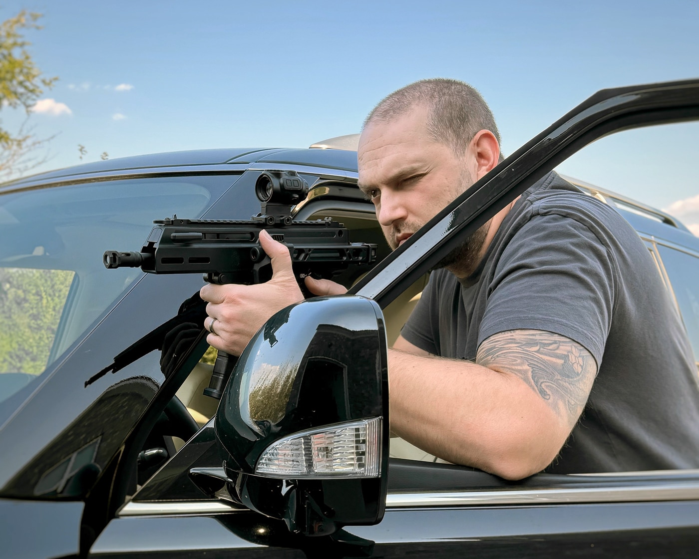 Shooter demonstrating Springfield Armory Kuna truck gun deployment from vehicle position showing practical defensive firearm usage scenarios. Vehicle defense training with Kuna pistol featuring roller-delayed operating system and folding brace for automotive shooting applications. Author testing truck gun performance from driver position illustrating real-world self-defense preparedness with Springfield Armory defensive firearm. Kuna 9mm pistol being fired from vehicle demonstrating flat-shooting characteristics and controllability in confined automotive spaces. Practical truck gun training showing proper handling of Springfield Armory Kuna with Strike Industries folding brace during vehicle-based scenarios. Defensive shooting practice with vehicle gun highlighting importance of familiarity with personal protection firearm before emergency situations. Springfield Armory Kuna truck gun usage demonstration showing compact design advantages for shooting from tight vehicle interior positions. Self-defense training session with Kuna pistol emphasizing hands-on experience necessary for effective truck gun deployment during actual threats.