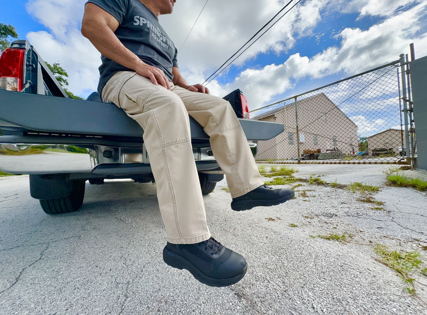 Law enforcement officer wearing Rocky Code Blue Public Service six-inch tactical patrol boots during field testing demonstration showing real-world police duty footwear application. Police officer in black Rocky Boots demonstrates ankle support and mobility provided by non-waterproof breathable mesh construction with TPU overlays for active patrol work. Tactical boots worn by experienced patrol officer with 25 years law enforcement experience including K9 handler and SWAT operations requiring durable duty footwear. Rocky Code Blue public safety boots shown in use providing context for police officers corrections officers and security professionals evaluating budget tactical footwear options. Six-inch patrol boots worn during circuit training workout including calisthenics burpees lunges and fence climbing exercises accelerating wear testing. Author wearing affordable $98 MSRP Rocky Boots demonstrating practical application of oil-resistant rubber outsole and EVA Rebound midsole cushioning during active duty simulation. Non-metallic tactical boots with removable Comfort Track footbed inserts worn by police professional showing comfortable fit requiring no break-in period. Rocky public service footwear tested through varied terrain including scrub brush drainage ditches and chain-link fence climbing representing real patrol scenarios for law enforcement officers.