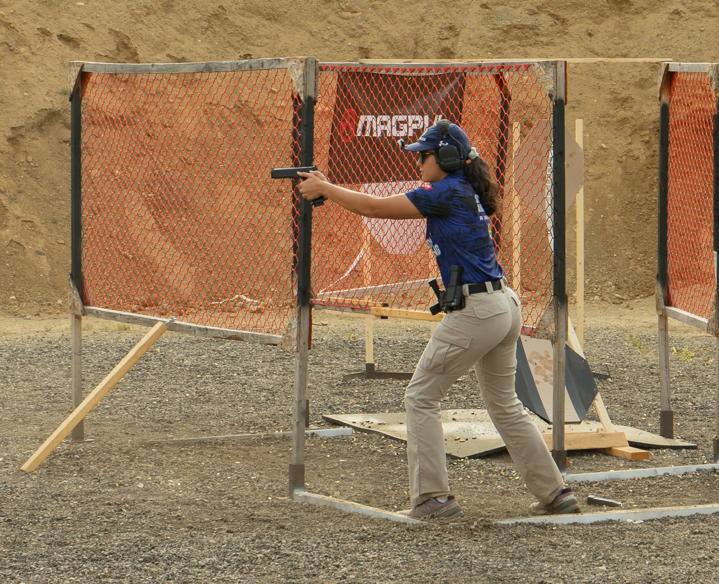 A collegiate shooting competitor actively engages targets during a timed stage at the 2025 USPSA Collegiate Action Pistol Championships hosted by the Hillsdale Chargers shooting team at the John A. Halter Shooting Center. The university action pistol athlete fires their handgun while moving through the course of fire at the Michigan range facility that attracted 13 competing teams. This competitive shooter demonstrates proper gun handling and marksmanship fundamentals during their stage run at the Hillsdale College championship match held at the Roger Ailes Action Pistol Shooting Center. The collegiate pistol competitor wears required safety equipment including eye protection and hearing protection while navigating one of the Springfield Armory sponsored stages. University shooting athletes like this competitor participated in either Limited or Limited Optics divisions at the Hillsdale competitive shooting event where teams from Texas A&M, Naval Academy, and Virginia Tech competed. The action pistol shooter's stage performance contributes to team scores in a match that has grown from eight teams in 2024 to 13 teams at the 2025 Hillsdale Chargers championship. This collegiate competitor represents the level of marksmanship skill displayed throughout the match where athletes demonstrated finest sportsmanship and professionalism regardless of school affiliation. The university shooter competes at a Hillsdale College facility that has established itself as a premier destination for USPSA collegiate action pistol championships.