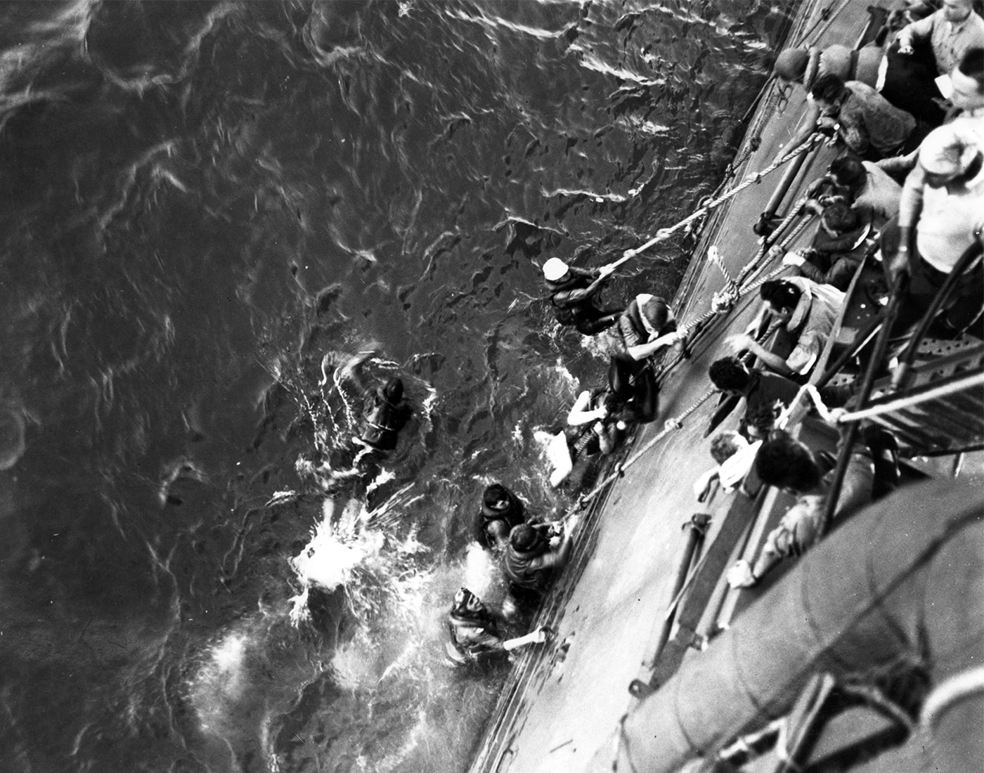 USS Lexington CV-2 crewmen being rescued and pulled aboard USS Minneapolis CL-36 after abandoning the burning aircraft carrier during the Battle of Coral Sea on May 8, 1942. Lady Lex survivors descended from lifelines into the warm waters of the Coral Sea after Captain Frederick C. Sherman ordered abandon ship in the late afternoon. More than 300 sailors evacuated the doomed Lexington carrier after two Type 91 torpedoes and multiple aerial bombs struck the converted battlecruiser causing uncontrollable fires. USS Lexington crew fought fires throughout the day but internal explosions knocked out engine room ventilators and threatened to detonate ordnance in hangar deck storage areas. Admiral Aubrey Fitch told Captain Sherman to get the men off the carrier after it became apparent the flattop couldn't be saved. Every living soul aboard USS Lexington CV-2 was rescued by escorting vessels including the New Orleans-class cruiser Minneapolis and destroyers, though 216 crew had been killed during Japanese attacks. Lady Lex Admiral Fitch and Captain Sherman were the last to leave the burning carrier. USS Lexington wouldn't sink despite the pounding and was finally torpedoed by destroyer USS Phelps to prevent capture by the Imperial Japanese Navy.