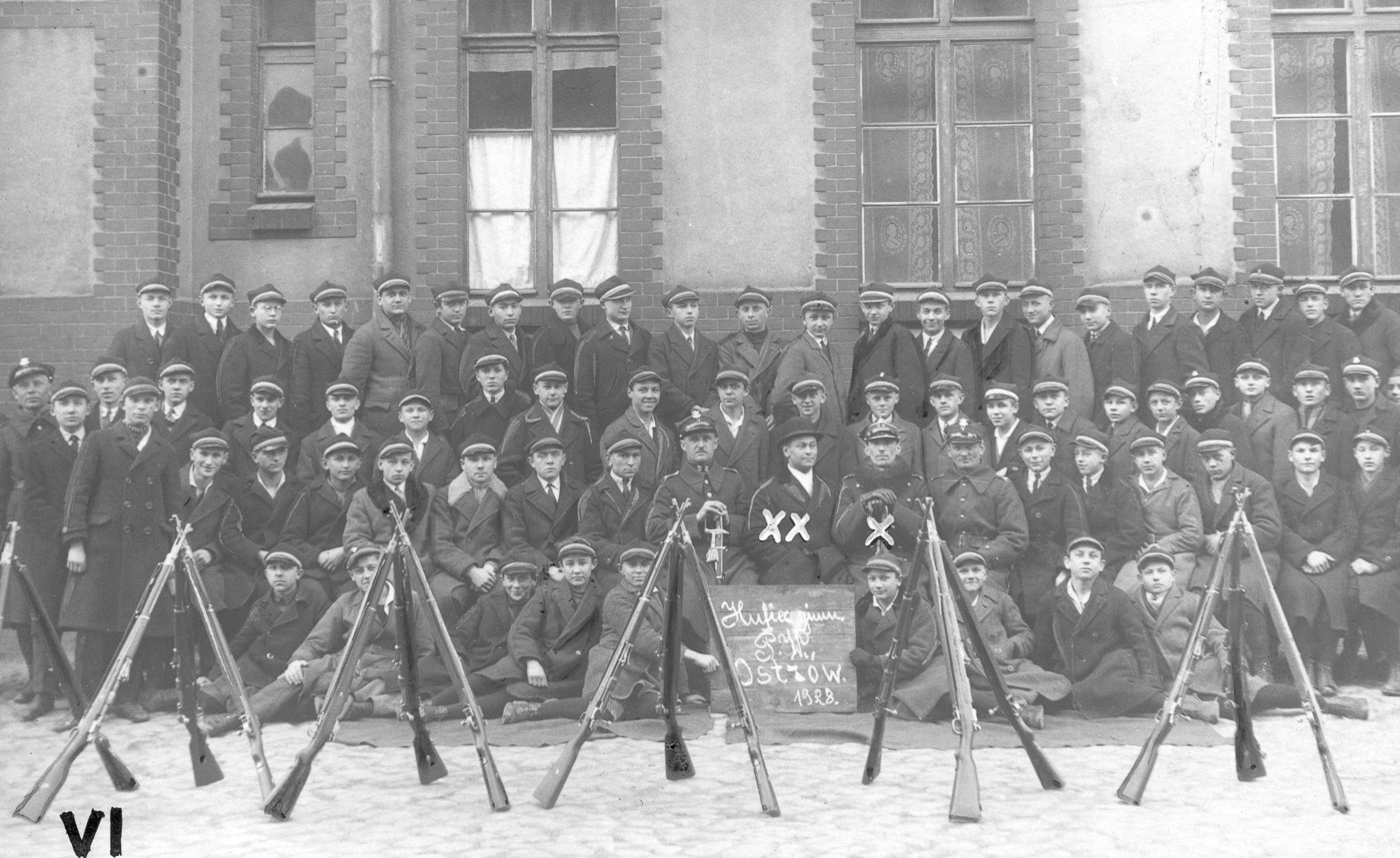 Formal group photograph of Polish Military Training Corps members posing with German Gewehr 98 bolt-action rifles showing organized Polish military training organization during interwar period between World War I and World War II. The uniformed Polish trainees hold Gew 98 rifles or Polish Mauser wz. 98 variants with characteristic 29-inch barrels, straight bolt handles, and full-length wooden stocks that became standard armament for Polish military training programs. These Polish Military Training Corps personnel armed with 7.92x57mm Mauser chambered rifles represent formalized preparation for national defense when Poland rebuilt military capabilities after gaining independence and faced threats from neighboring powers during 1920s-1930s. The group displays Gewehr 98 rifles featuring reliable controlled-feed Mauser action, five-round internal magazines, and robust construction that made German G98 design ideal for training future Polish soldiers in marksmanship and military tactics using same bolt-action rifle system that equipped millions of German Imperial Army infantry during Great War.