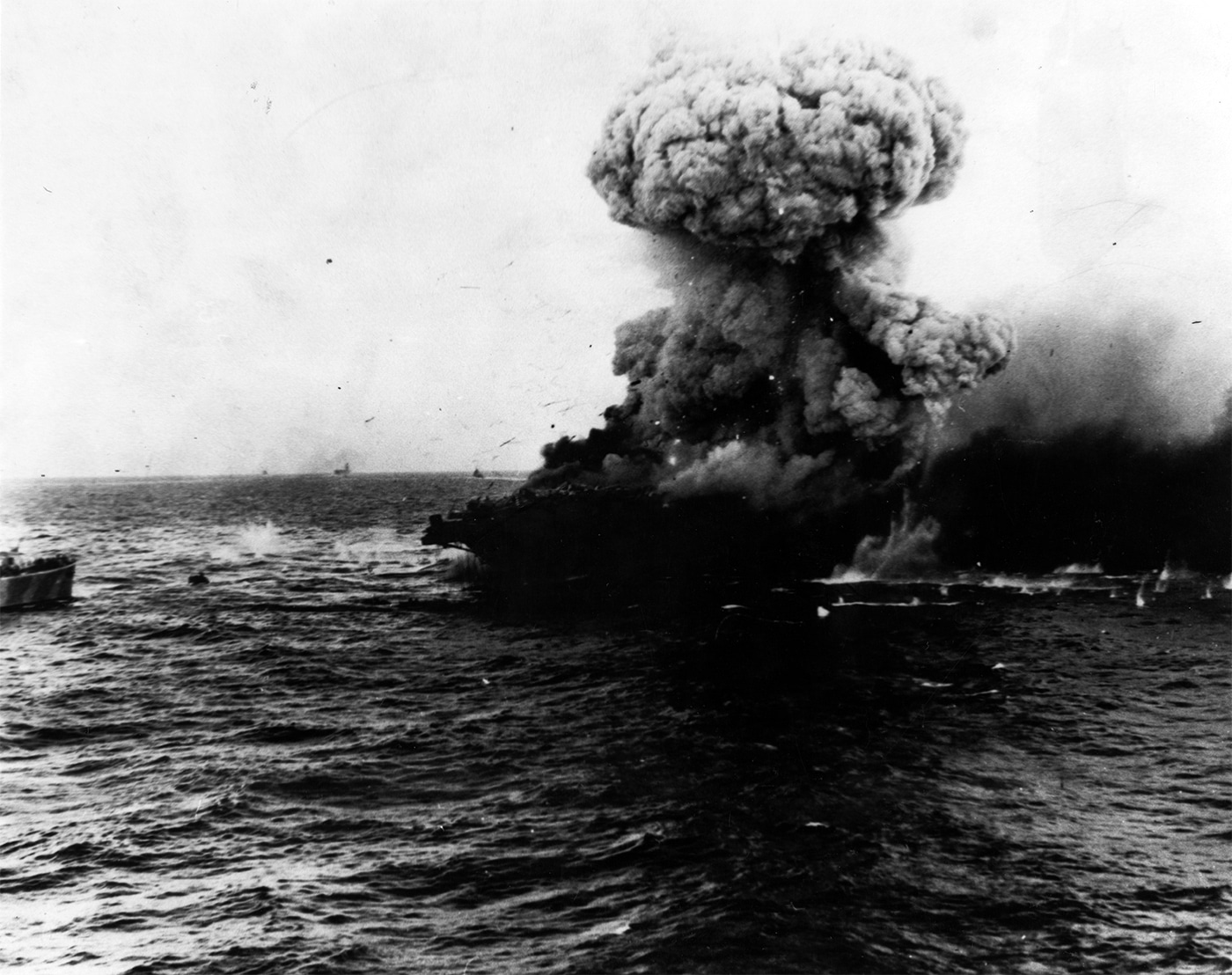 Massive mushroom cloud rising from USS Lexington CV-2 after a catastrophic explosion aboard the burning aircraft carrier on May 8, 1942 during the Battle of Coral Sea. This tremendous explosion probably resulted from torpedo warheads stored in the starboard side of the hangar aft detonating at approximately 1727 hours following an earlier explosion amidships. Lady Lex had been fighting uncontrollable fires since being struck by two Type 91 torpedoes at 1120 hours and multiple aerial bombs from Imperial Japanese Navy aircraft. USS Lexington CV-2 crew spent hours battling flames throughout the converted Lexington-class battlecruiser carrier but internal explosions knocked out engine room ventilators. The Lexington aircraft carrier explosion from detonating torpedo warheads created this mushroom cloud visible for miles across the Coral Sea. This devastating blast convinced Admiral Aubrey Fitch and Captain Frederick C. Sherman that USS Lexington couldn't be saved despite heroic damage control efforts. The carrier was abandoned shortly after this explosion with more than 300 sailors evacuating into the Coral Sea before being rescued by USS Minneapolis and destroyers. Lady Lex became the first United States Navy fleet aircraft carrier lost in World War II after earning two battle stars during five months of Pacific combat.