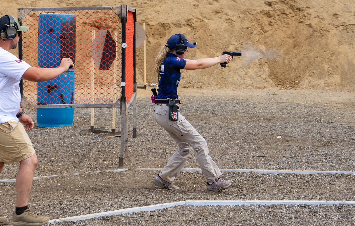 A competitive shooter fires their pistol at targets during a stage at the 2025 USPSA Collegiate Action Pistol Championships hosted by the Hillsdale Chargers shooting team at the John A. Halter Shooting Center in Michigan. The action pistol competitor demonstrates proper shooting stance and gun handling fundamentals while engaging targets during their timed run at the Hillsdale College championship match. This shooter wears required eye and ear protection while firing through one of the courses at the Roger Ailes Action Pistol Shooting Center that features six pistol bays and a 100-yard rifle range. The competitive athlete represents one of the many shooters from 13 university teams including Texas A&M, Naval Academy, Virginia Tech, Michigan State, and Oklahoma State competing at the Hillsdale Chargers facility. Pistol competitors like this shooter participated in either Limited or Limited Optics divisions using various firearms platforms at the Hillsdale competitive shooting event sponsored by Springfield Armory and other industry partners. The action shooter's performance during this stage contributes to individual and team scores in a match that grew from eight teams in 2024 to 13 teams at the 2025 Hillsdale College championship. This competitive pistol athlete demonstrates the marksmanship abilities developed through collegiate shooting programs that gather at the Hillsdale Chargers facility for USPSA action pistol competition. The shooter competes at a Hillsdale College range that has established itself as a driving force in university-level practical shooting sports championships.