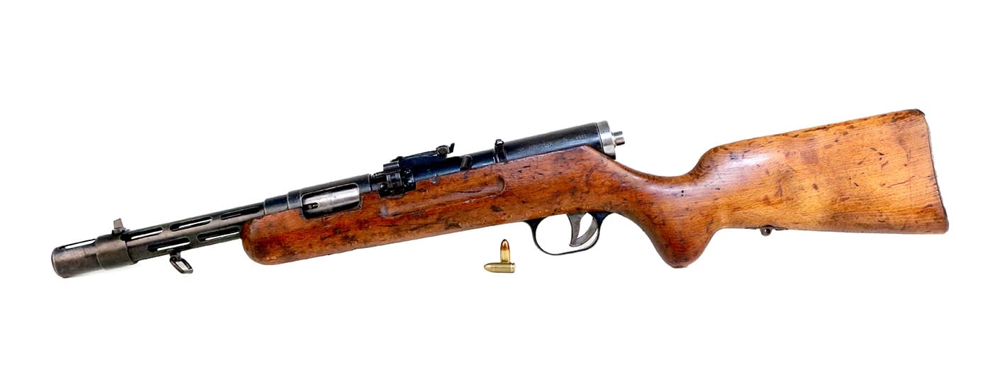 A left-side profile view of the Bergmann MP35 submachine gun showing the ejection port, machined receiver, and overall weapon architecture from this perspective. MP35 ejection occurred on the left side. Bergmann weapons featured asymmetric designs. The MP35 submachine gun utilized side-feeding magazines. German firearms incorporated unusual layouts. SS troops adapted to MP35 configuration. The Bergmann MP35 combined unique design elements. Waffen SS soldiers operated left-ejecting weapons. This submachine gun demonstrated distinctive engineering choices.