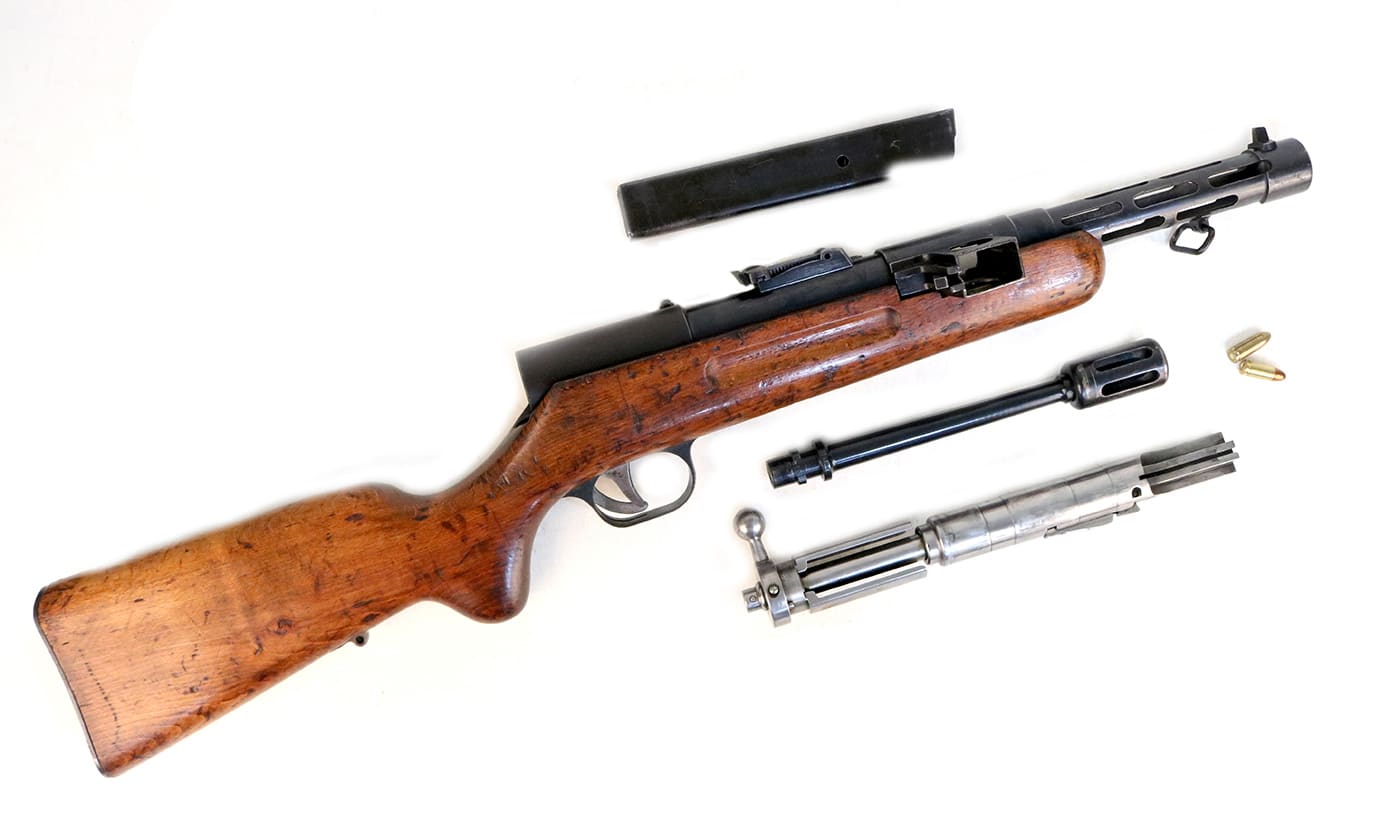 A completely disassembled Bergmann MP35 submachine gun with all major components laid out systematically, including the receiver, bolt assembly, barrel, magazine, and various internal parts. MP35 components required precise machining. Bergmann firearms utilized complex assemblies. The MP35 submachine gun incorporated multiple safety mechanisms. German weapons demanded skilled manufacturing. SS armories maintained MP35 systems regularly. The Bergmann MP35 featured rotating bolt designs. Waffen SS gunsmiths serviced these firearms. This weapon's internals demonstrated interwar engineering complexity.