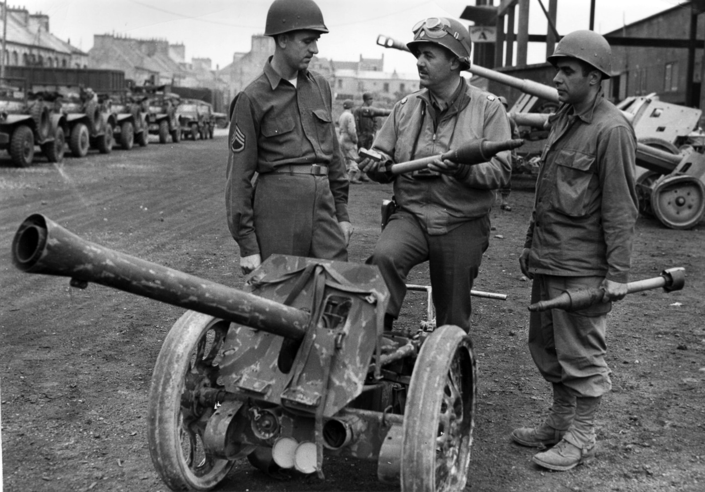 American soldiers in World War II uniforms gather around a captured 8.8cm Raketenwerfer 43 Püppchen anti-tank rocket launcher on display somewhere in France. US forces captured German rocket weapons in Europe. Allied troops examined enemy anti-tank launchers. The Püppchen was a prized intelligence find. American soldiers encountered German rocket technology. The Raketenwerfer 43 interested US ordnance experts. GIs inspected captured Wehrmacht equipment. Allied intelligence studied German hollow charge weapons. The 88mm rocket launcher was displayed for troops.
