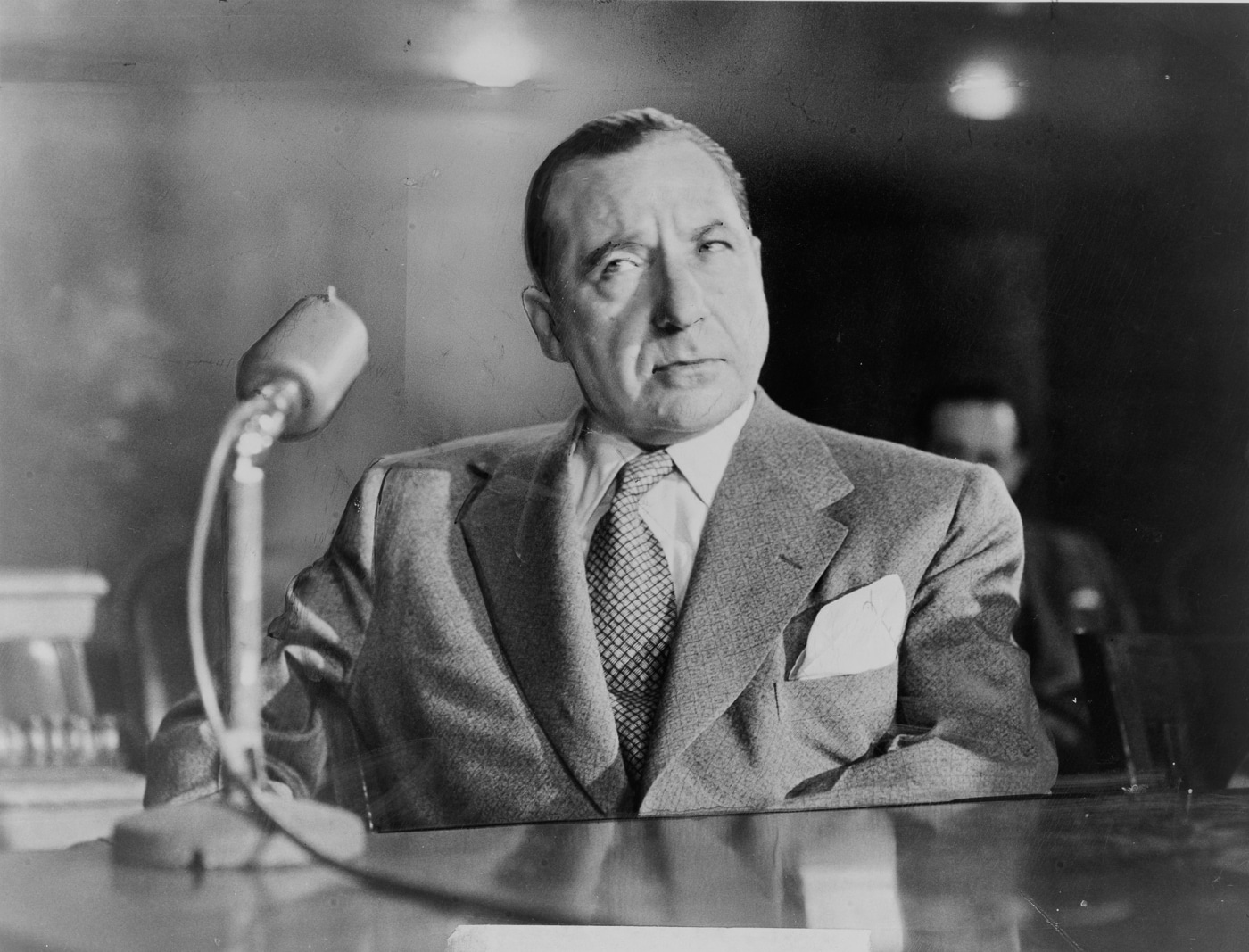 Frank Costello sits before microphones at a congressional hearing table in 1951, his hands prominently featured as cameras avoided showing his face during testimony. Operation Underworld benefited from Costello's extensive political network and influence. Mafia role in World War II included behind-the-scenes coordination with municipal authorities. Costello served as acting boss after Vito Genovese fled. His Tammany Hall connections enabled quiet cooperation between criminals and law enforcement. Criminal leaders shielded the operation from unwanted public scrutiny effectively. Costello became acting boss when Luciano appointed him in 1937. The collaboration required political finesse blending criminal authority with governmental needs. Costello's contributions helped legitimize the unconventional wartime partnership successfully.