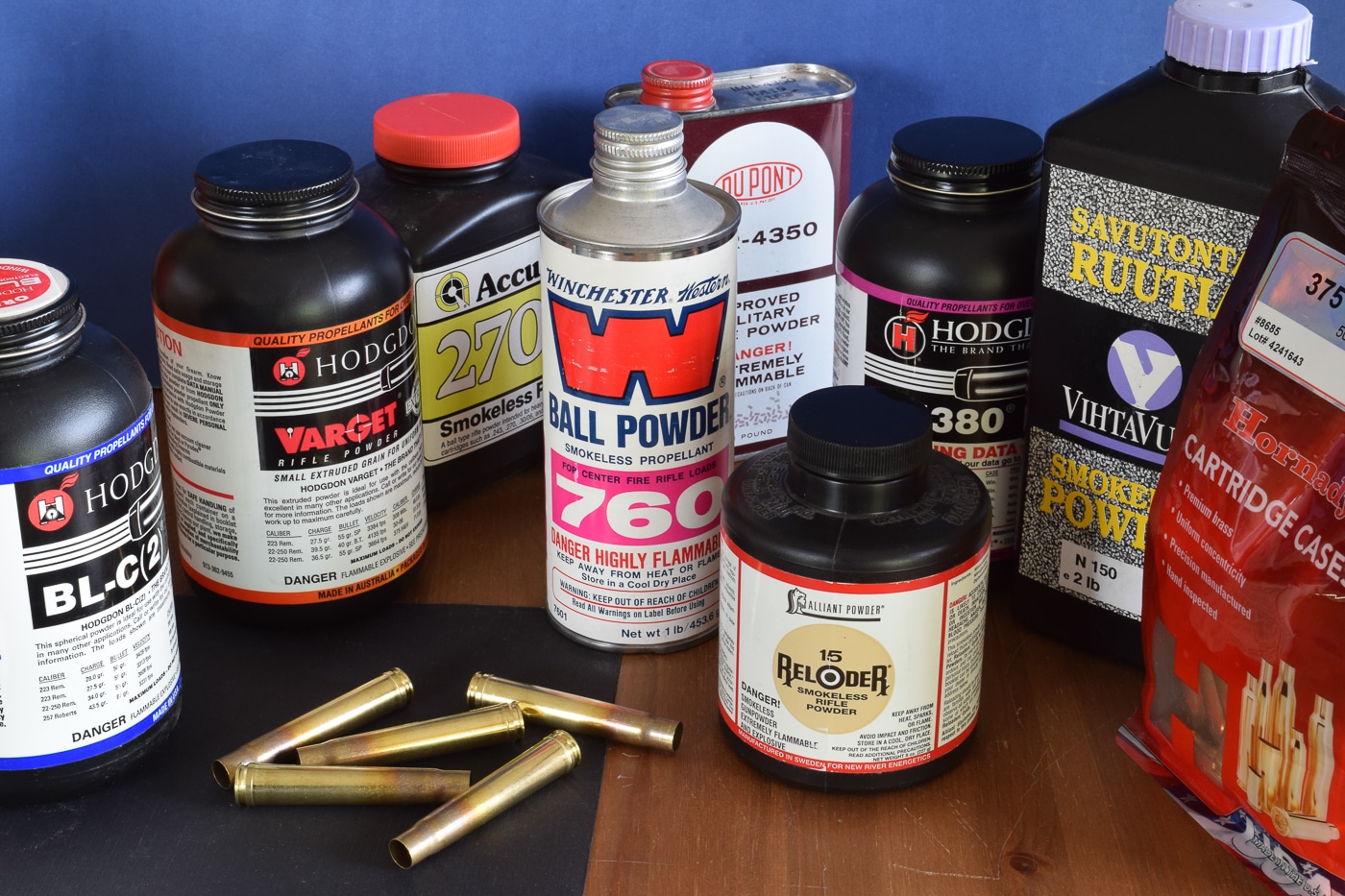 A photograph displays numerous containers of various gunpowder brands including Hodgdon, IMR, Winchester, Accurate, and Ramshot products arranged together, representing the extensive portfolio of propellants controlled by Hodgdon Powder Company totaling over 120 different formulations. Gunpowder history reflects industry consolidation trends. Hodgdon began with surplus military propellants. Origins of gunpowder distribution involved entrepreneurial acquisition. Bruce Hodgdon purchased IMR business in 2003. Multiple powder brands operate under one company. Gunpowder origins evolved through commercial partnerships. Winchester powders use licensing agreements. Ancient propellant markets lacked such consolidation.