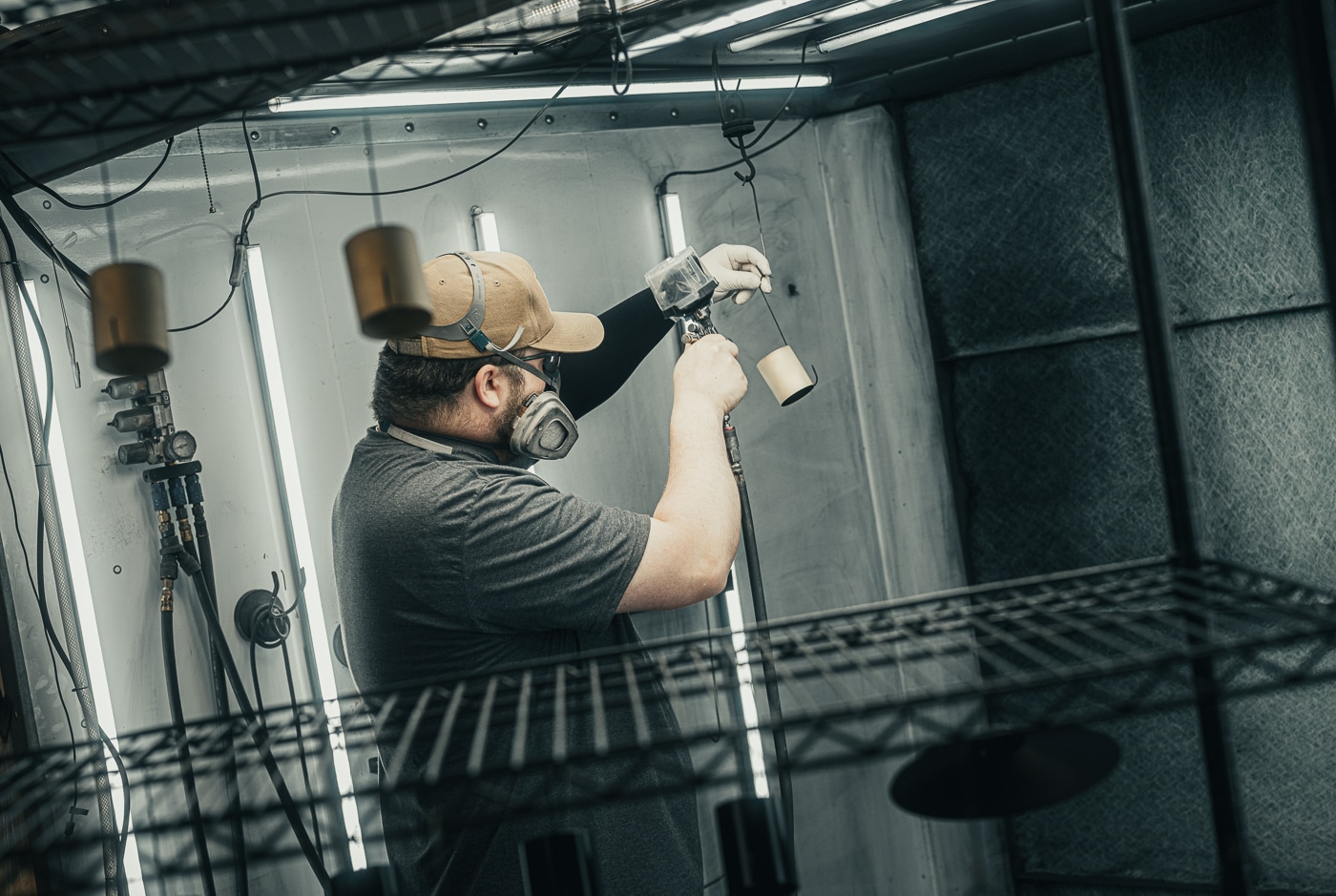 A person wearing protective equipment applies custom finishing coating to firearm components at a professional workstation with proper ventilation and tools. The Koted interview highlights hands-on craftsmanship importance. Koted Custom Finishings maintains manual precision standards. Interview of Koted discusses team expertise investment. Cerakote application requires specialized skill sets. Koted interview reveals chemistry knowledge integration. Finishing processes ensure repeatable quality results. The interview of Koted covers bench-level execution excellence. Koted balances automation with human craftsmanship.