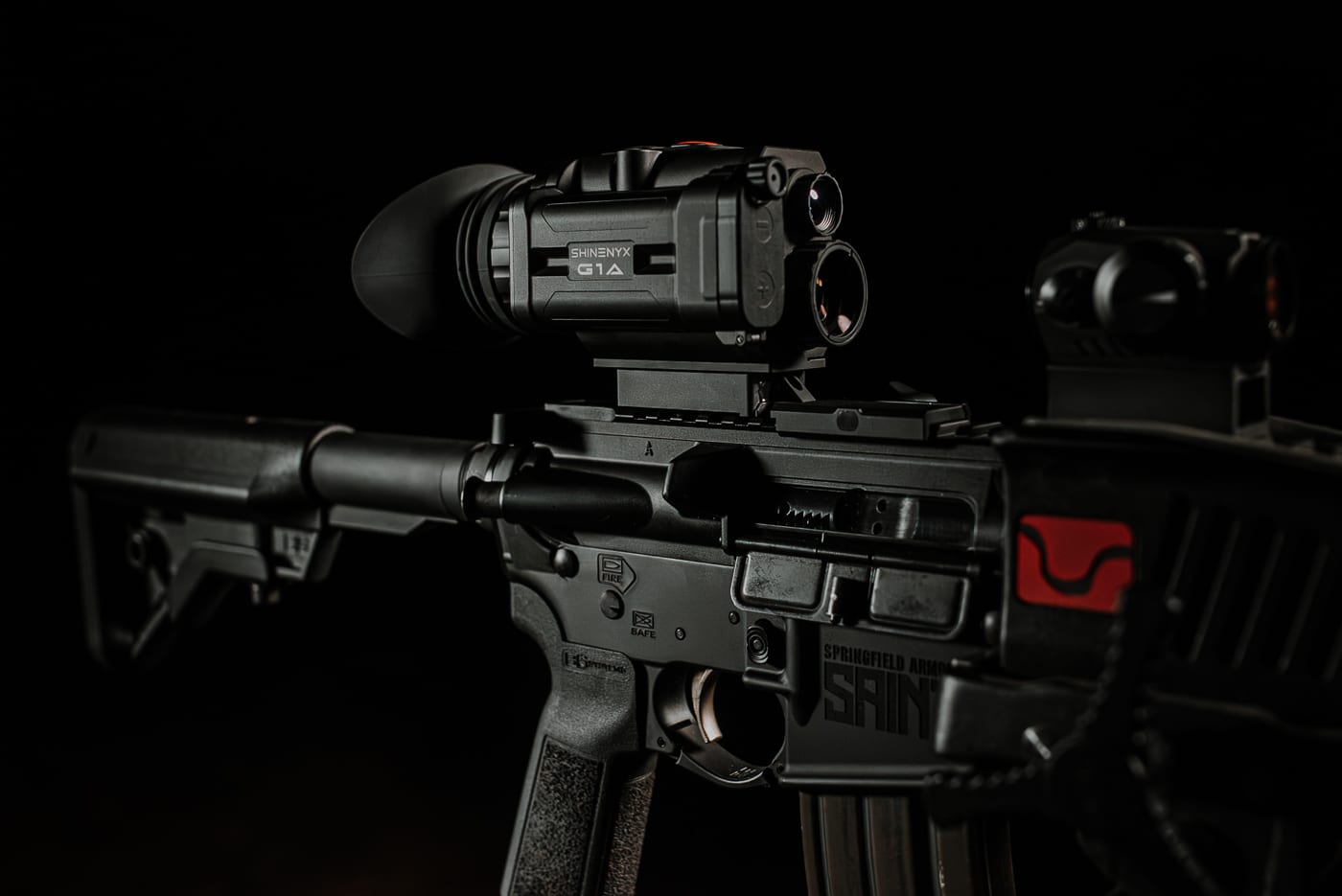 A tactical rifle equipped with the Shinenyx G1A monocular, modern optic, and accessories displaying a complete night-capable weapon system on dark background. The Shinenyx G1A review showcases complete system integration. Modern rifles accommodate multiple accessory attachments. Fusion monoculars enhance low-light shooting capability significantly. Shinenyx night vision gear complements existing optics naturally. Tactical setups benefit from thermal detection additions. Night-capable weapons improve operational effectiveness dramatically. The G1A weighs only seventeen ounces total. Integrated systems provide comprehensive situational awareness enhancement.