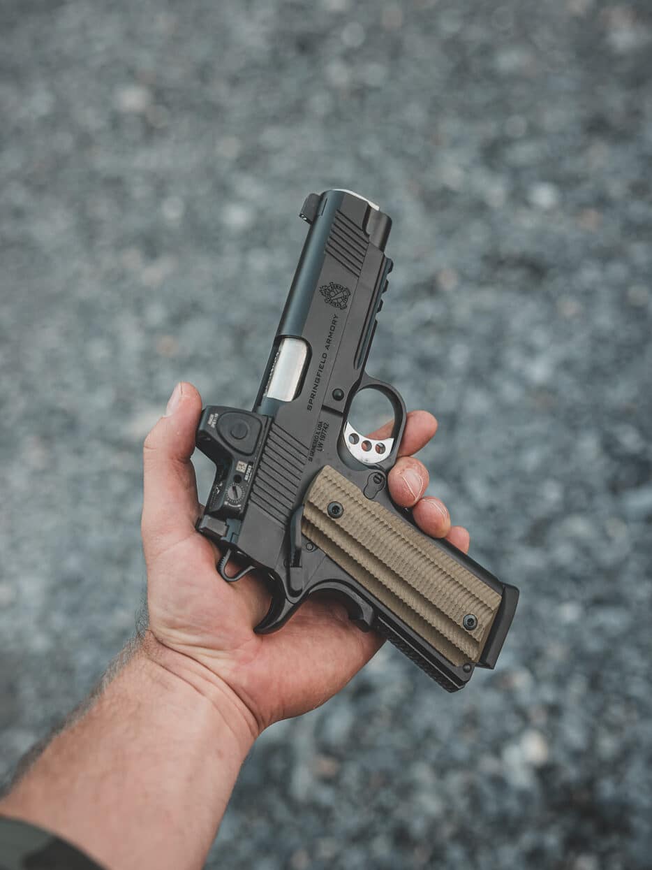 A photograph shows the Springfield Armory Operator 1911 pistol equipped with a mounted red dot optic for self-defense applications. The 1911 pistol's strengths include modern accessory compatibility. Red dot sights accelerate target acquisition speed. Optics-ready slides don't compromise core mechanics. Self-defense shooters benefit from enhanced accuracy. The 1911 pistol's weaknesses add optic-related considerations. Mounted sights increase overall pistol height. Battery dependency creates potential failure points. Quality optics require proper installation torque.