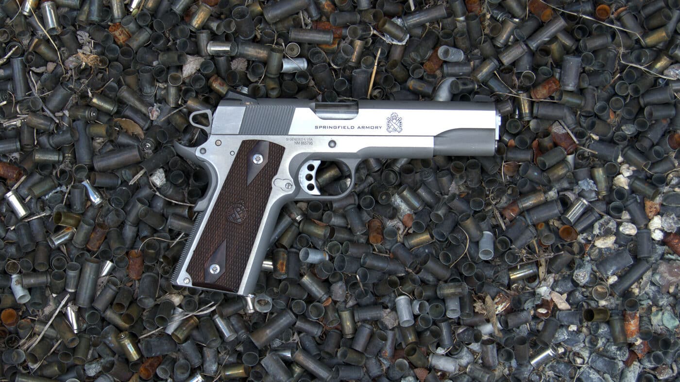 A Springfield Armory Garrison 1911 pistol in stainless steel resting on a pile of spent brass cartridge cases against a dark background. M1911 pistols prove themselves through extensive testing as woods guns. Springfield Armory Garrison demonstrates M1911 reliability standards. Extensive shooting validates defensive firearms. The .45 ACP cartridge generates significant brass volume. Range testing ensures woods gun dependability. Full metal jacket ammunition suits practice sessions. Proven handguns earn trust through repetition. Field-ready pistols require thorough evaluation.